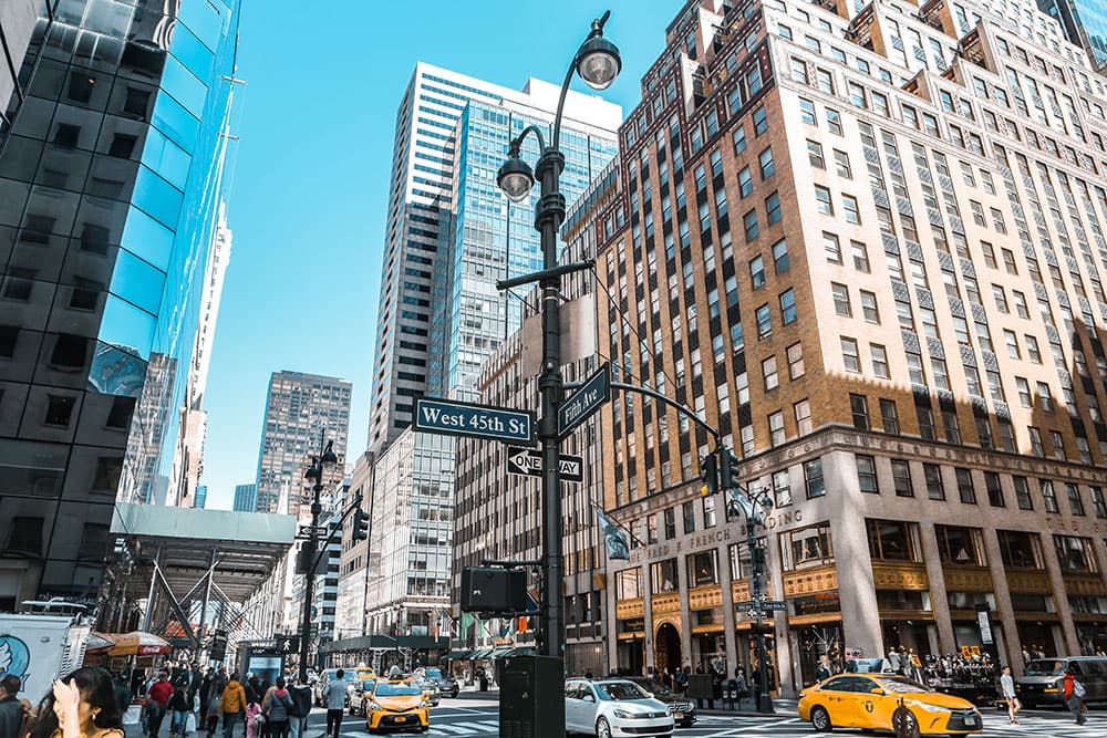 new york city street yellow taxi crowds of people tall buildings brown and glass