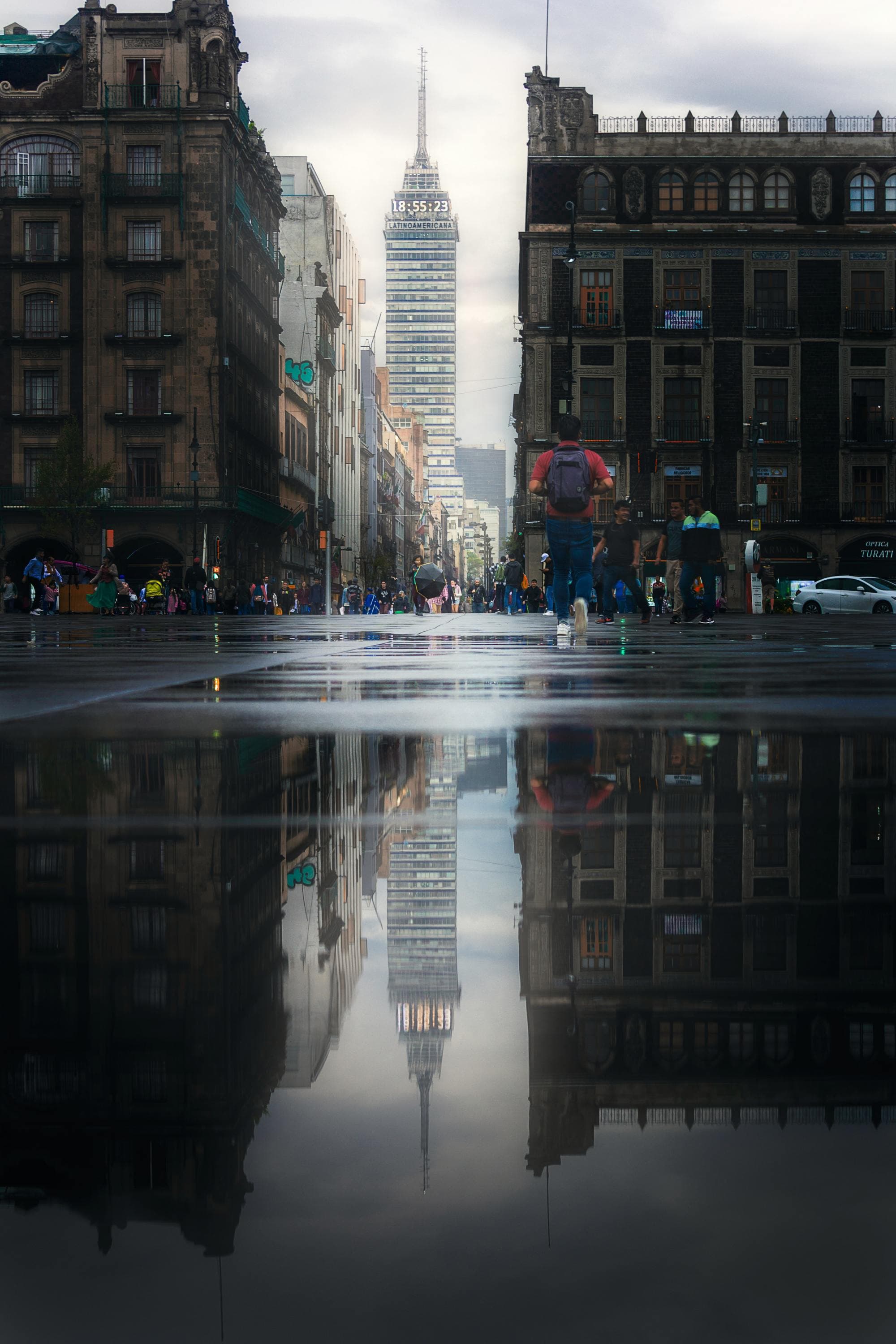 rainy day in a city, a tall building reflects in the puddle in an open plaza