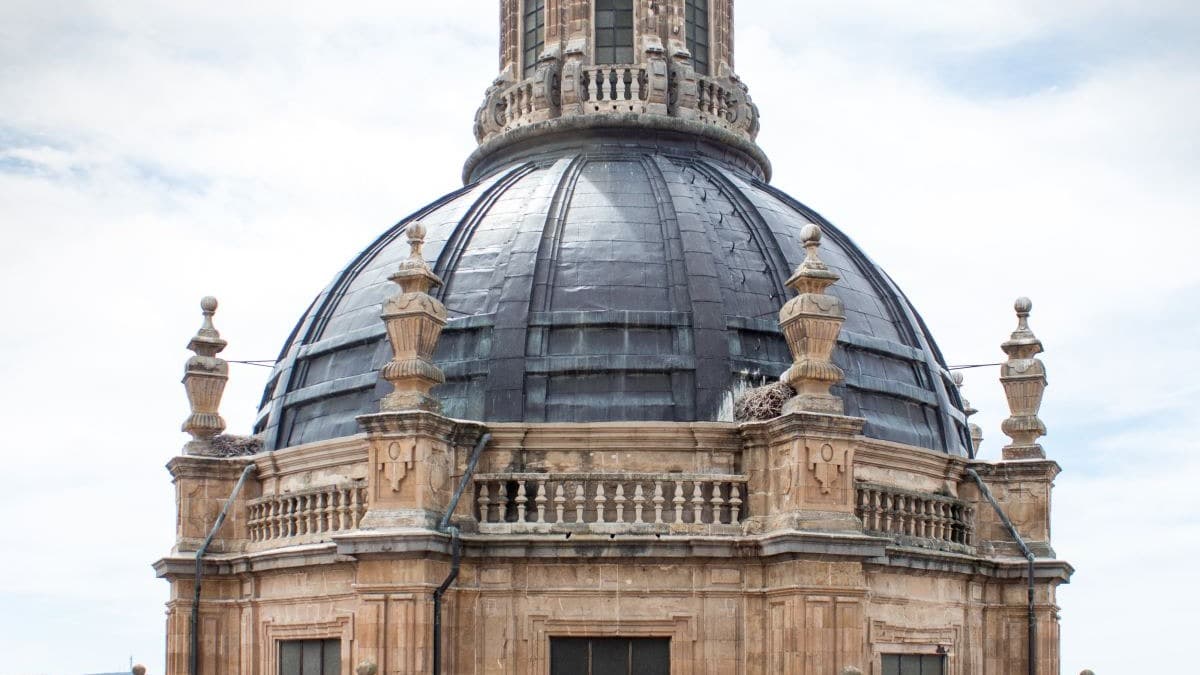 A beautiful old stone building with a dome roof and a spiral at the top with a cloudy blue sky in the background.