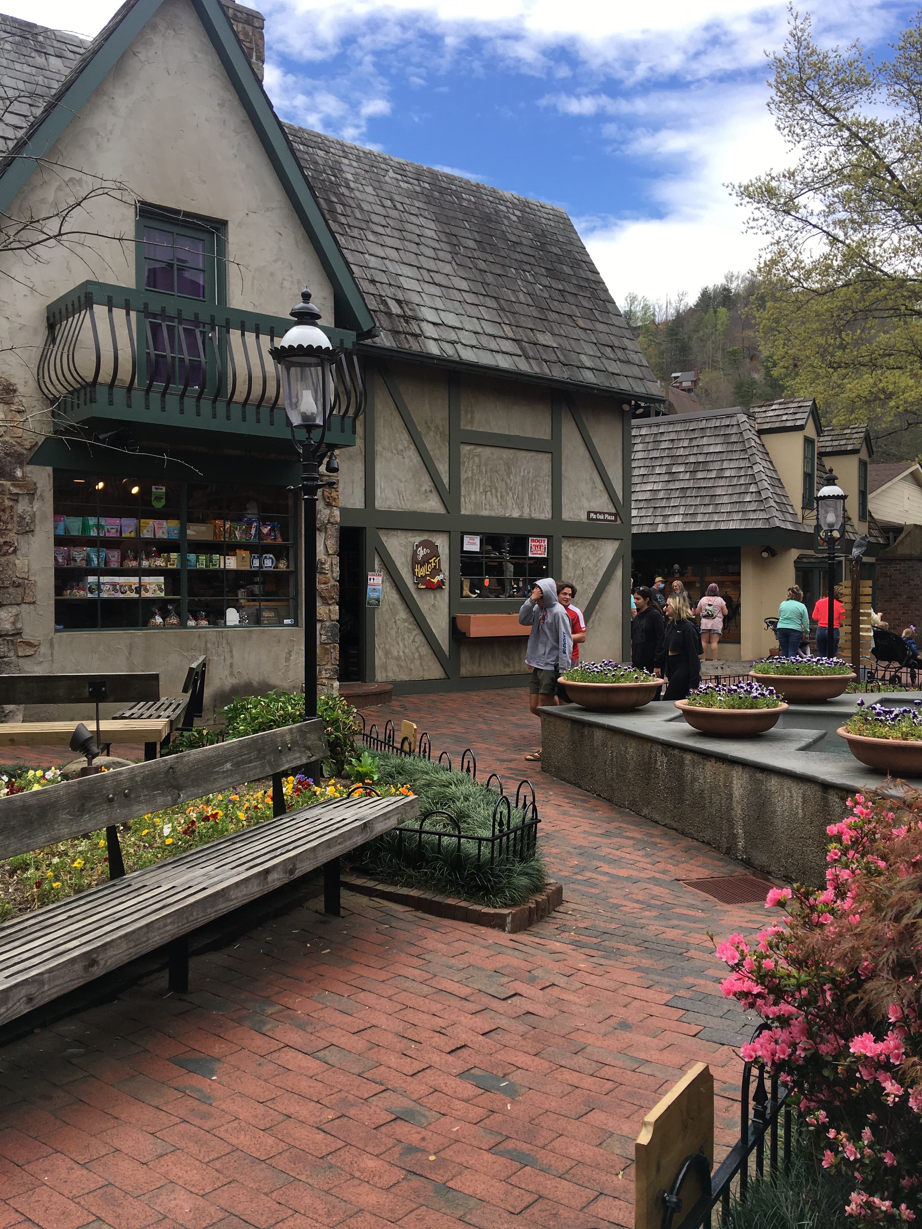 A red brick town square with stone buildings and flowers, with hills in the background