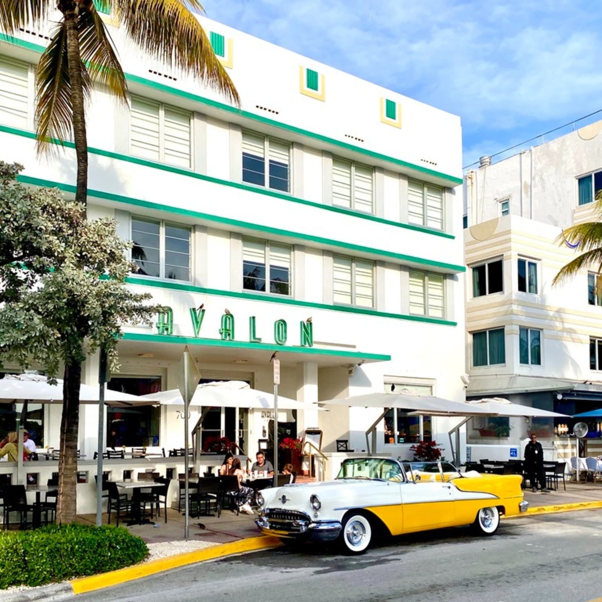 A picture of the street with a vintage yellow car parked in front of a white and green building