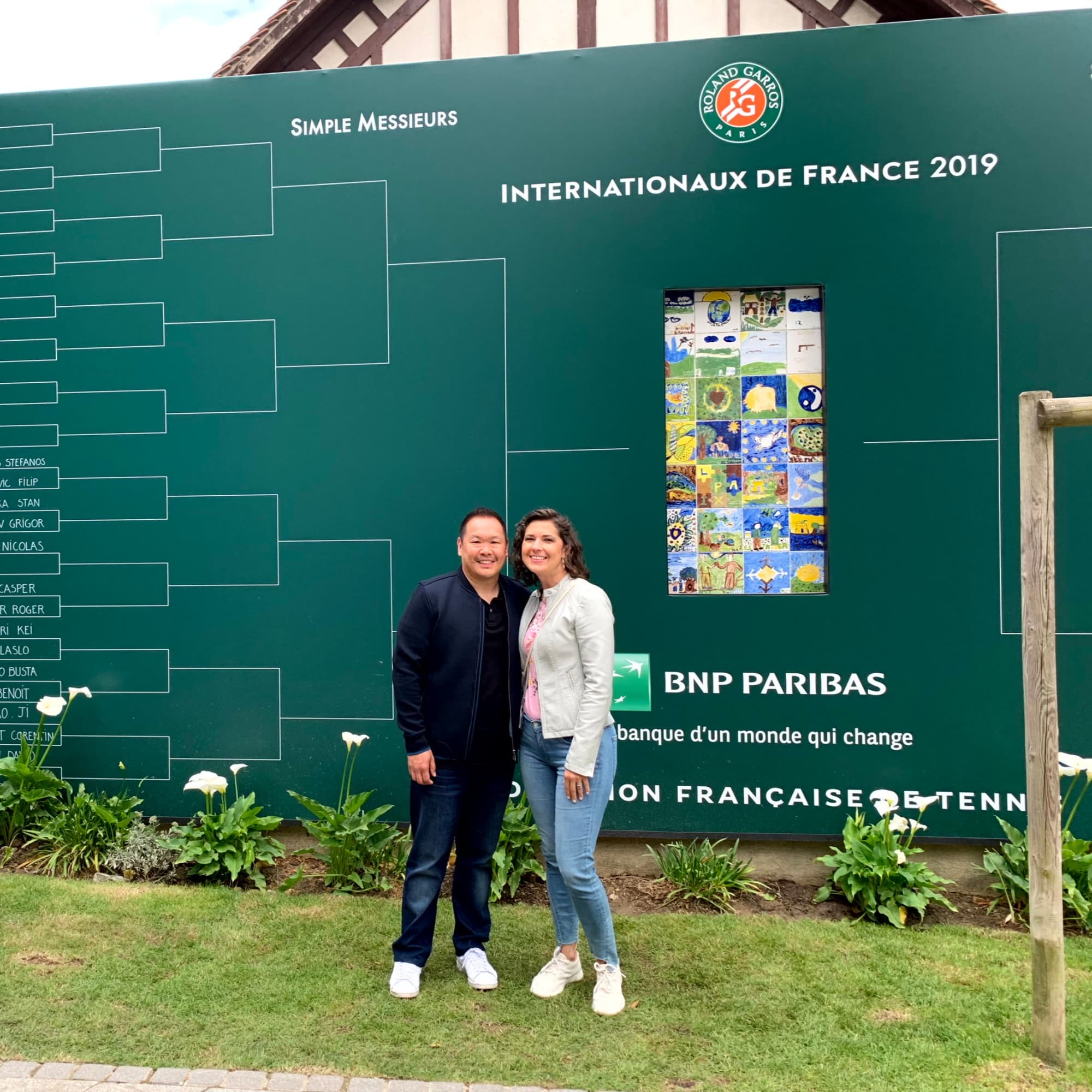 A couple standing in front of a large green sign that reads Internationaux de France 2019.