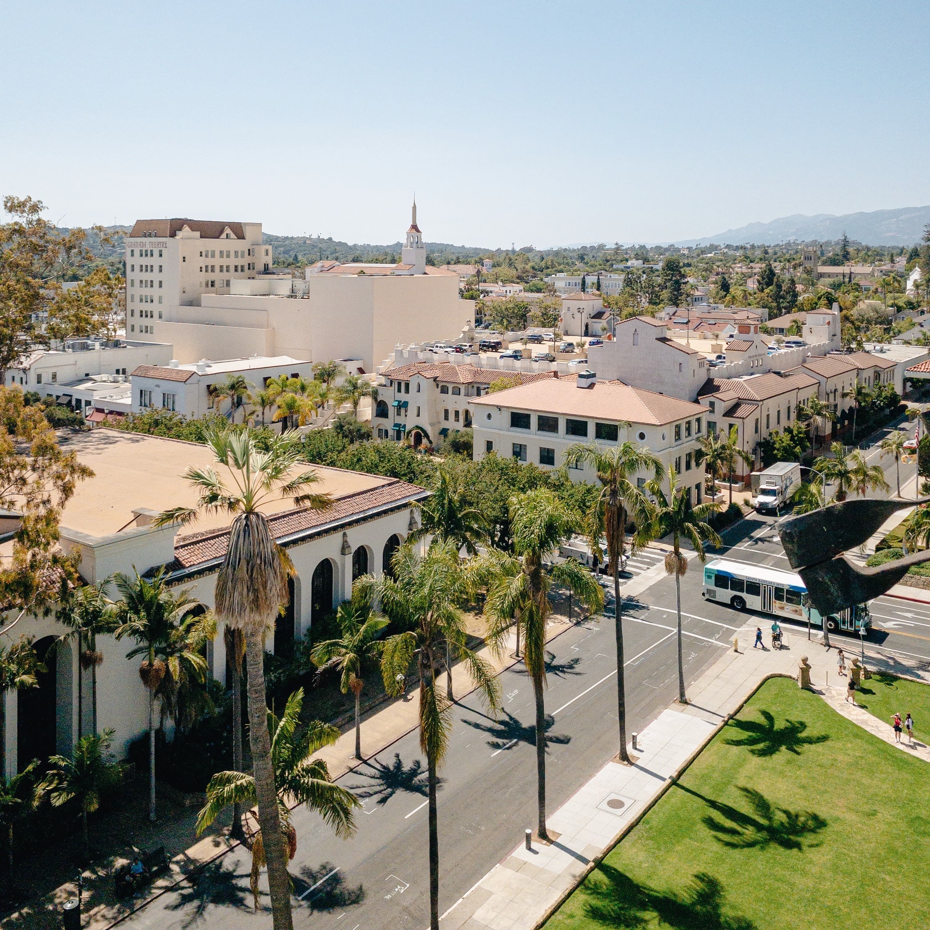 An aerial view of white buildings with pink roof tops and palm trees.