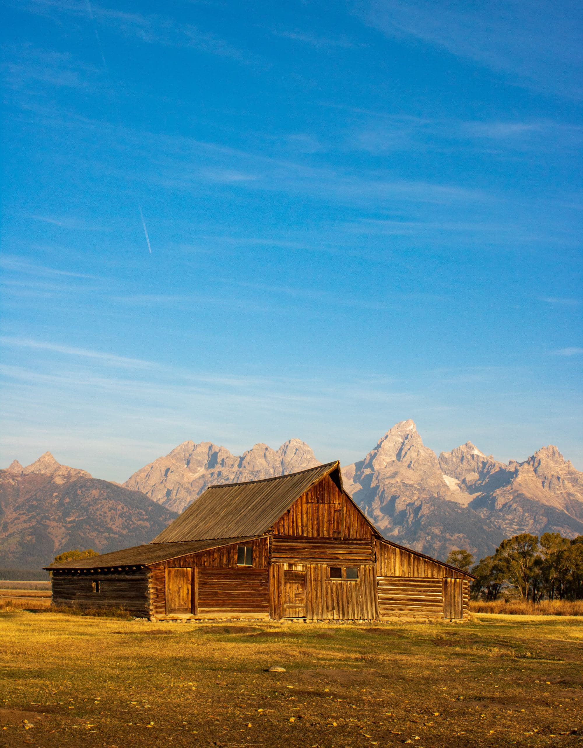 historic barn on the flats beneath a vast mountain range with a clear blue sky above