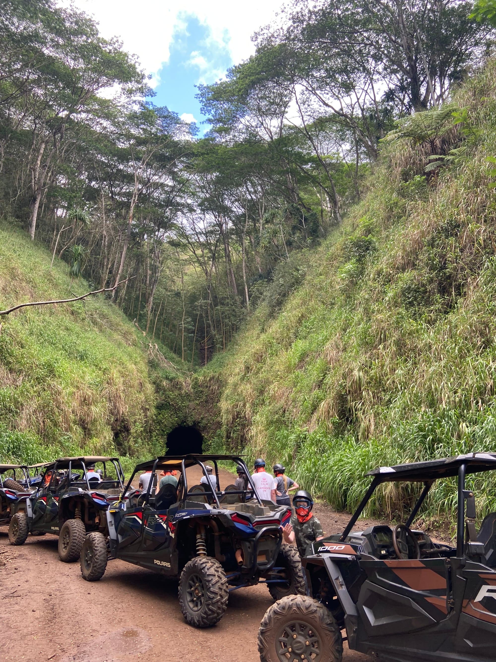 A row of black jeeps in a hilly area near tunnel.