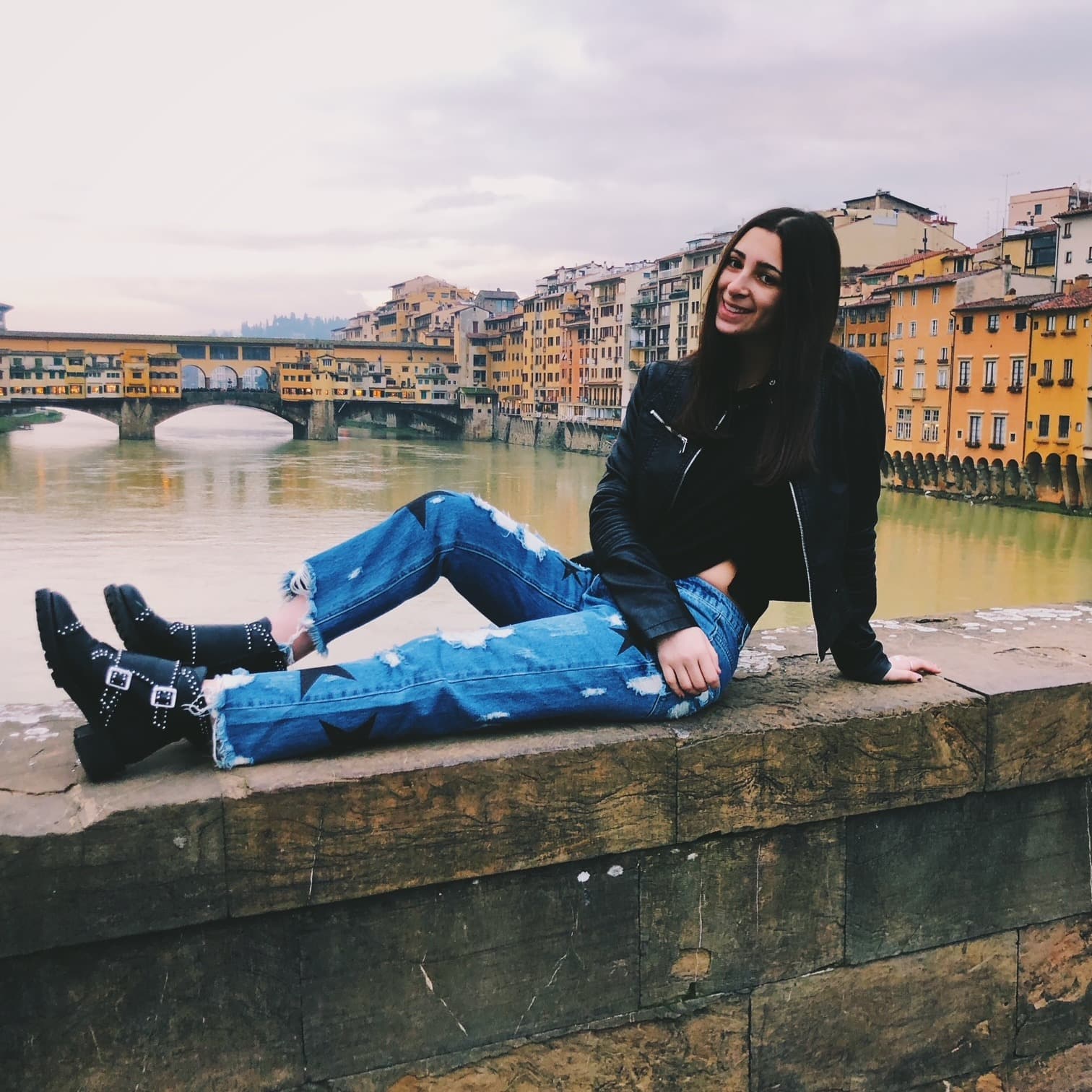 A woman in blue jeans and black jacket near city canal.