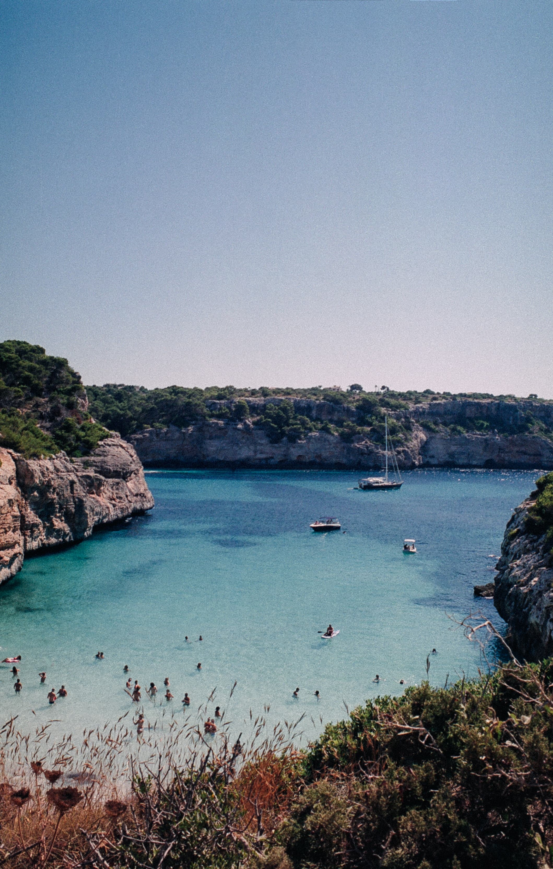 people swimming in a beach surrounded by rocks during daytime