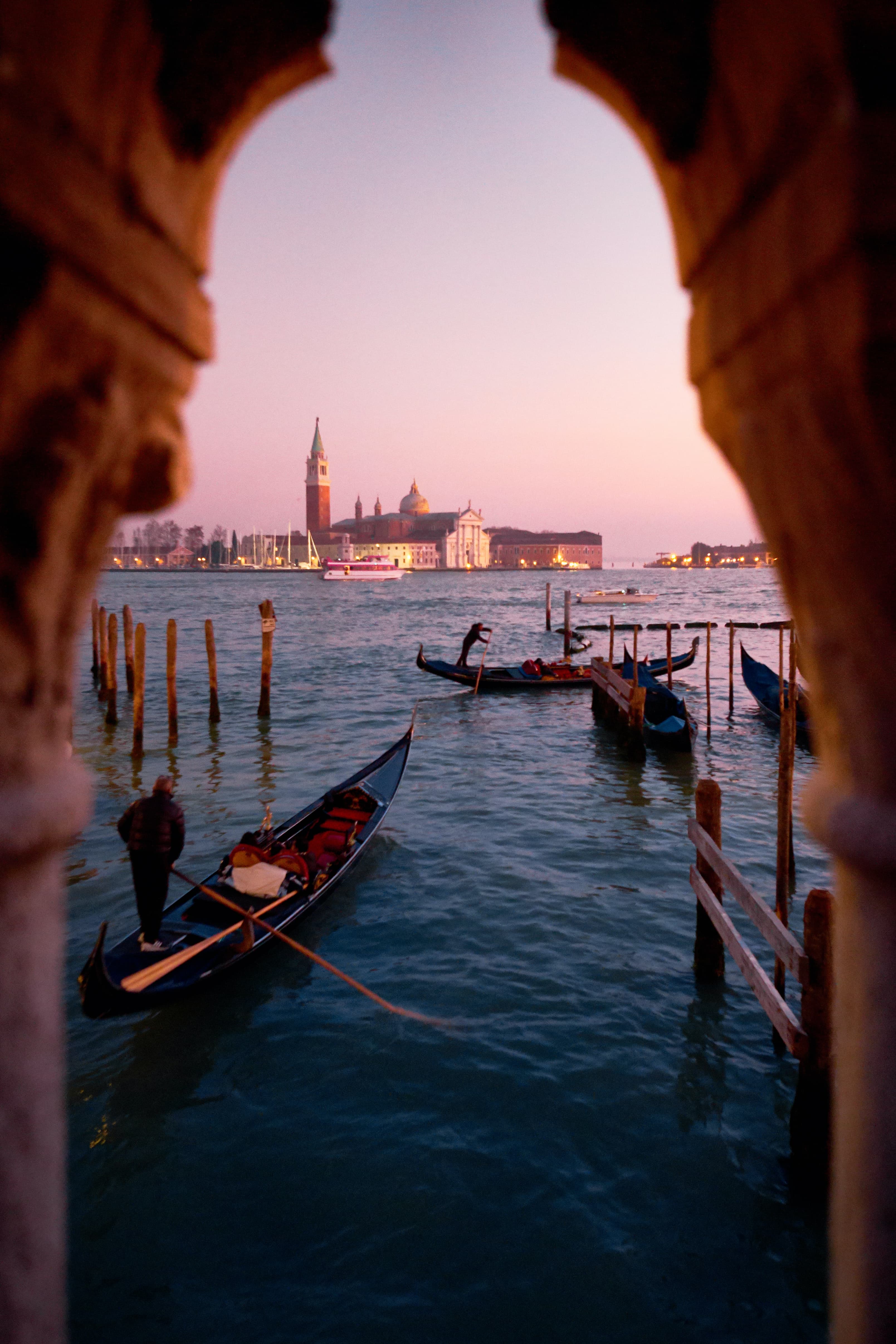 boats in a body of water with buildings in the background during sunset