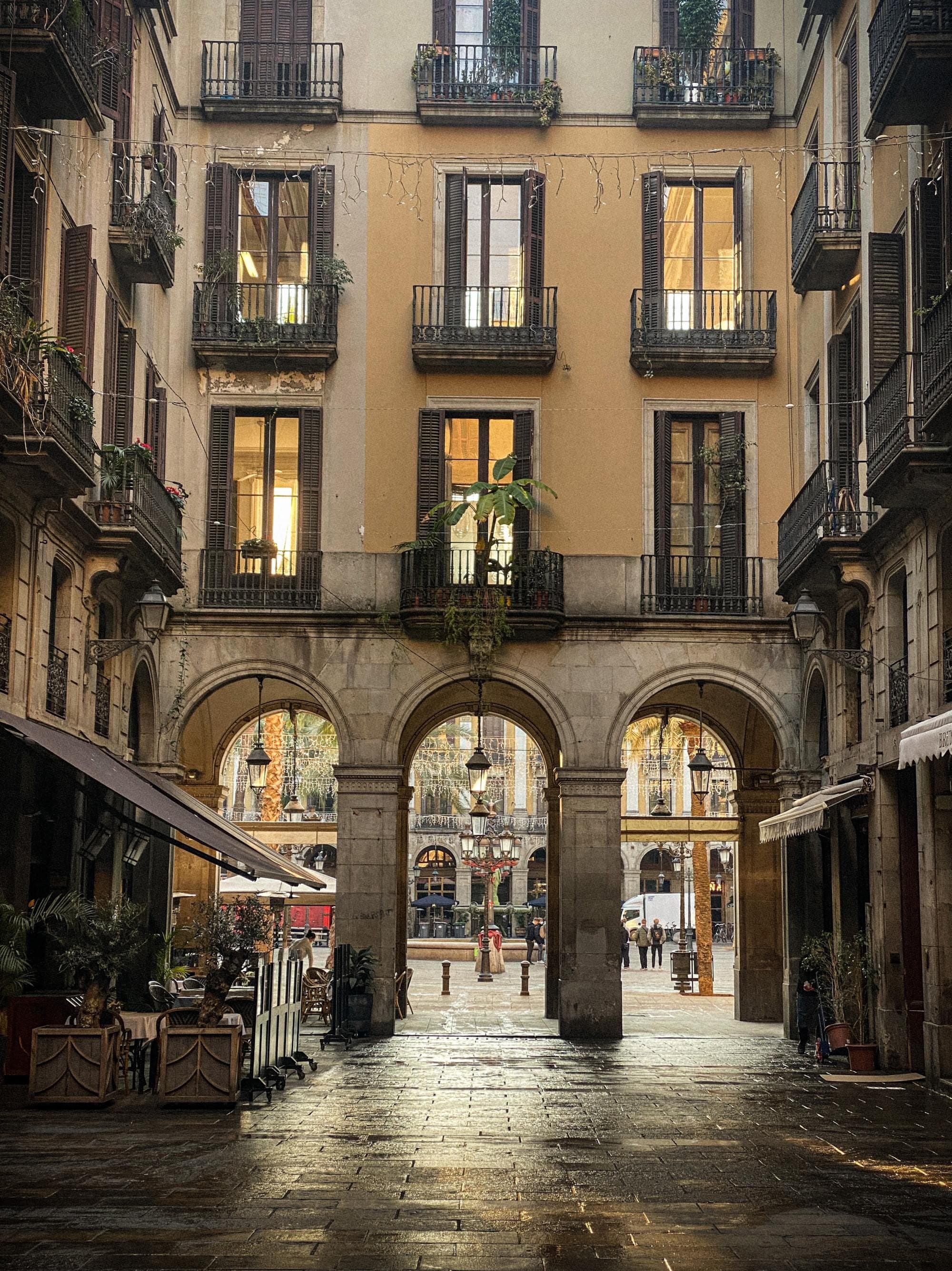 view through arch ways under lit up windows to an open plaza with wet stone ground from rain