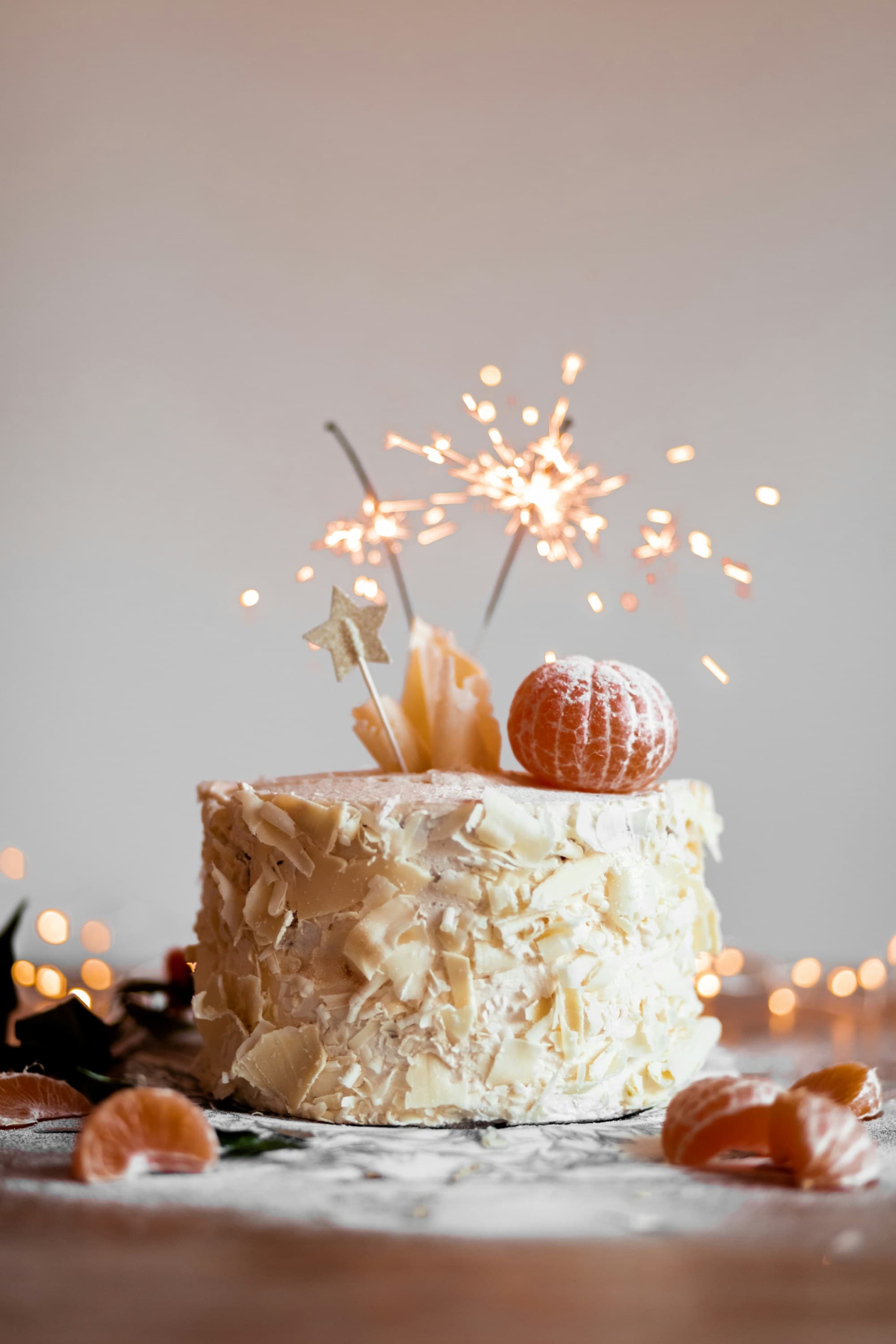 A cake with white frosting, peeled oranges and sparkling candles.