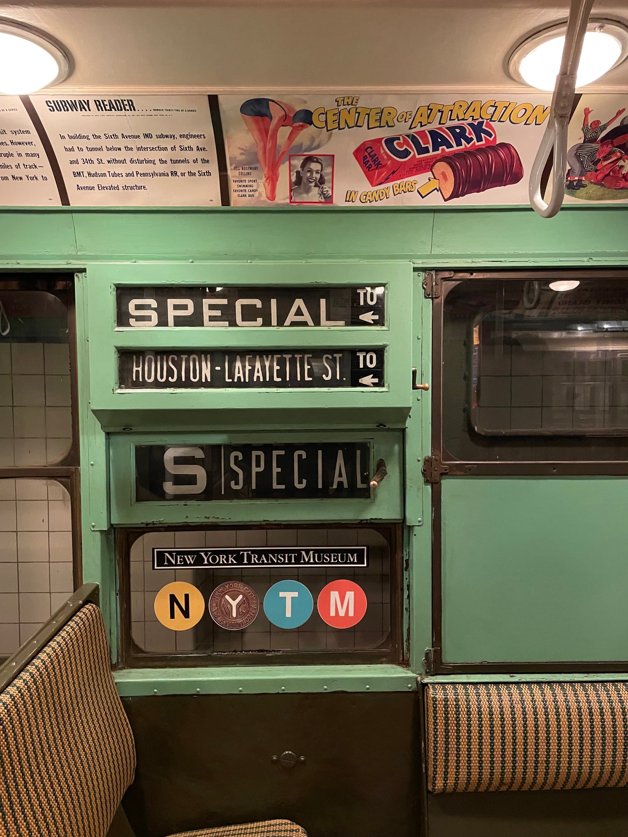 The focus is on a green wall with a window. Above it, signs indicate the train’s route and stops, including “HOUSTON ST / VARICK ST.”