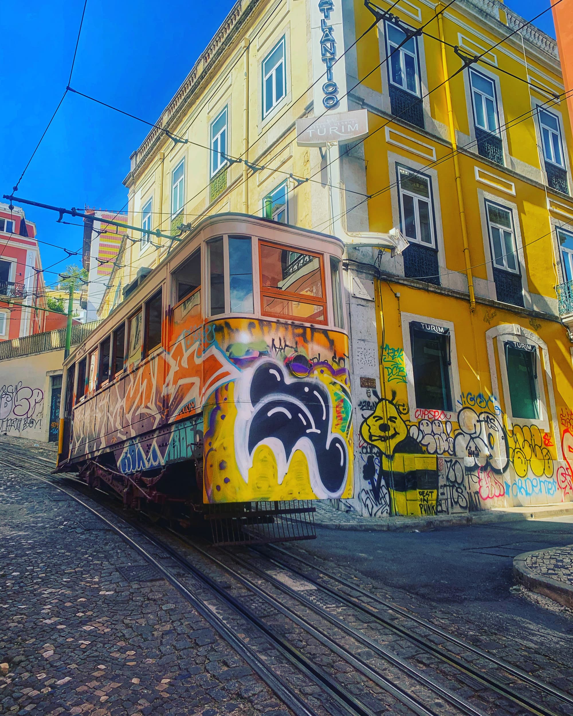 A yellow tram near a yellow building on the road during daytime.