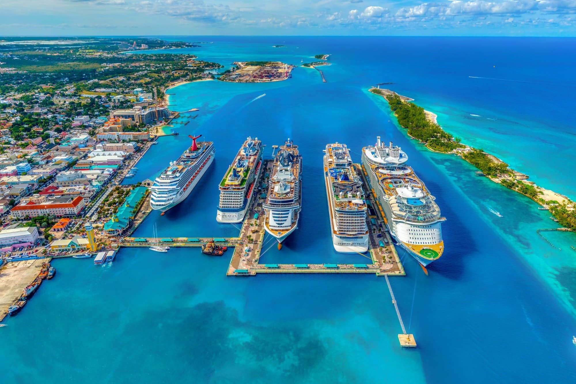 Five cruise ships, including a liner belonging to the Virgin Voyages fleet, are docked at a port in the Bahamas on a sunny day with sapphire blue waters contrasting with the rainbow of colors displayed in the port (photo by Fernando Jorge)