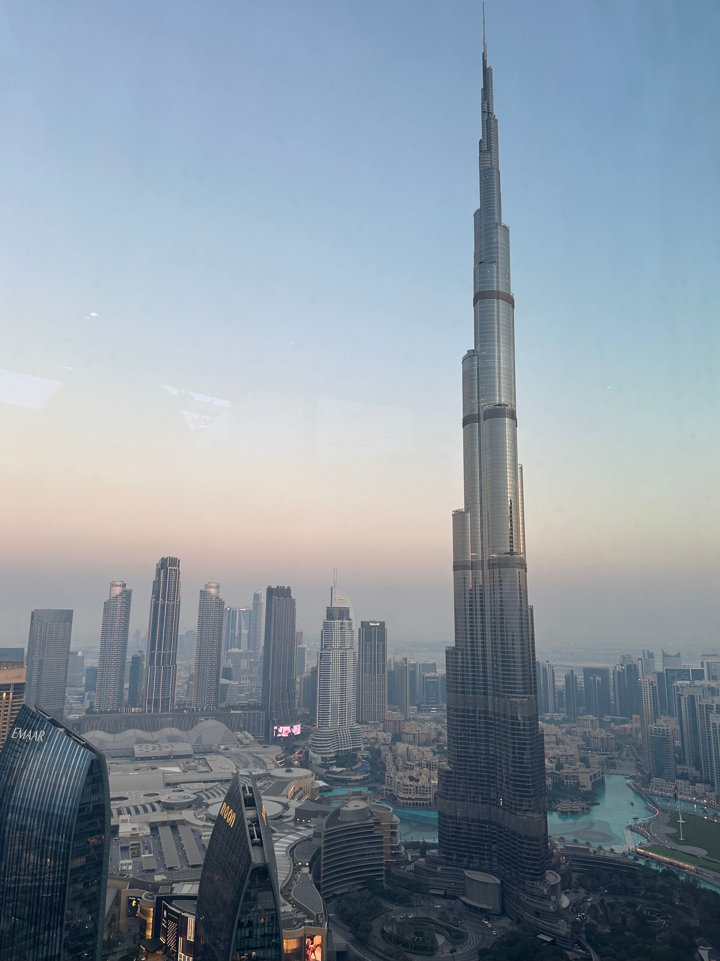 A view of the tallest skyscraper in Dubai with a large cityscape in the background. There is a faint sunset in the background too.