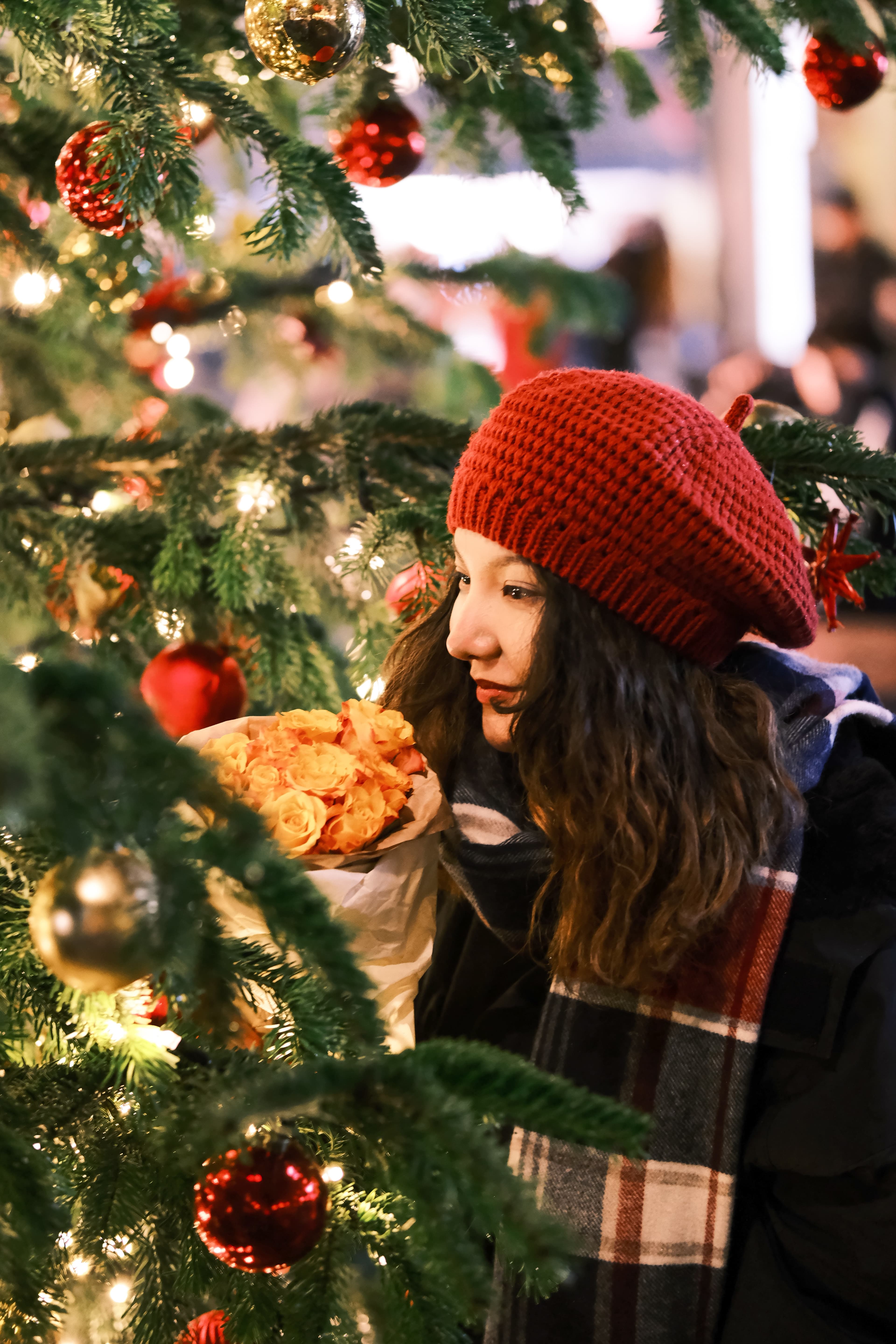 A girl in a red hat standing next to a Christmas tree at a market.