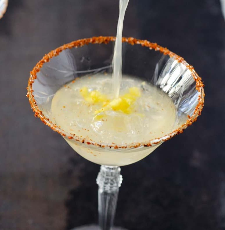 Delicious margaritas being poured in a coup glass with a spicy salt rim.