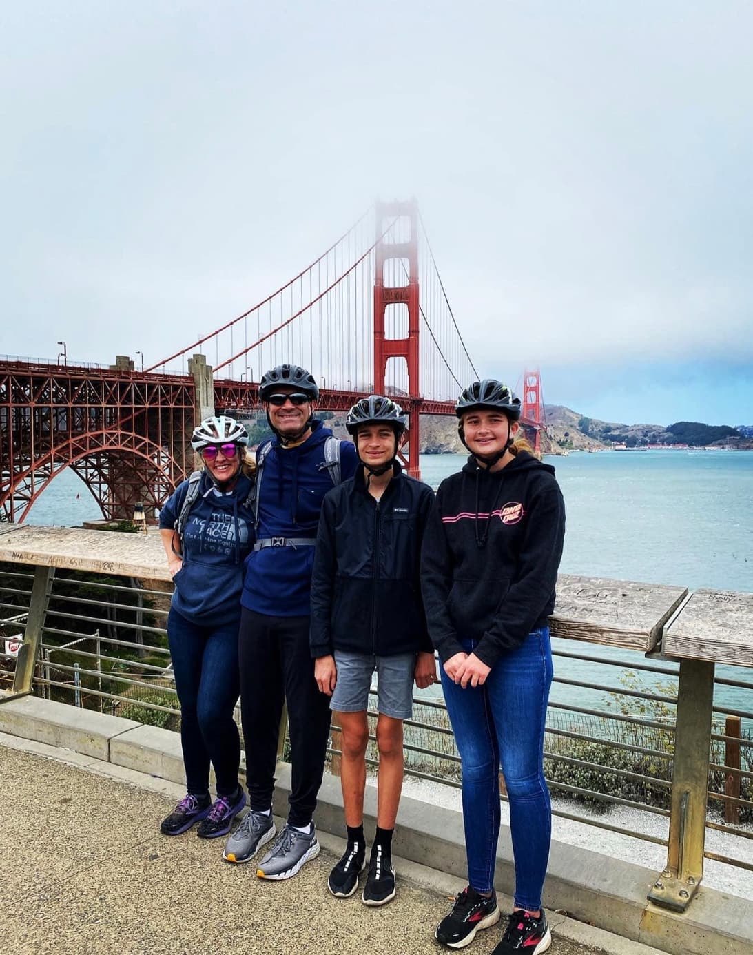 A family wearing helmets posing in front of the Golden Gate Bridge on a cloudy day.