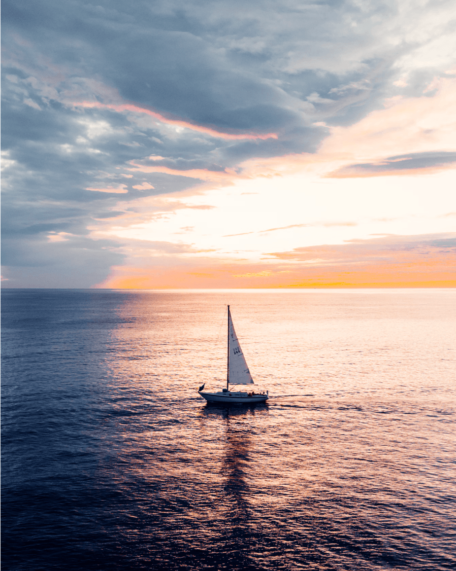 A view of a sailboat at sunset over the water.