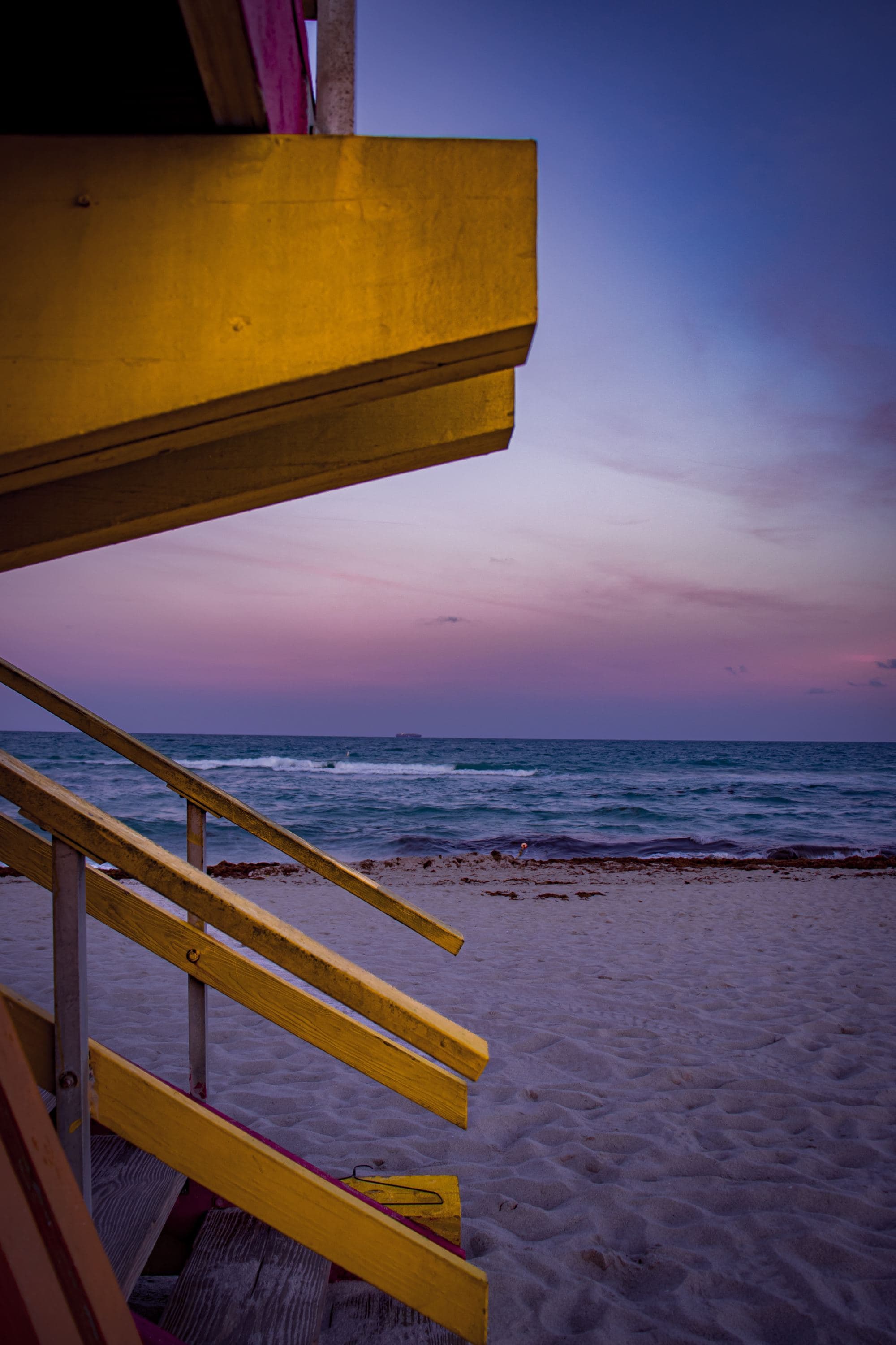 purple sunset on the beach next to yellow lifeguard stand