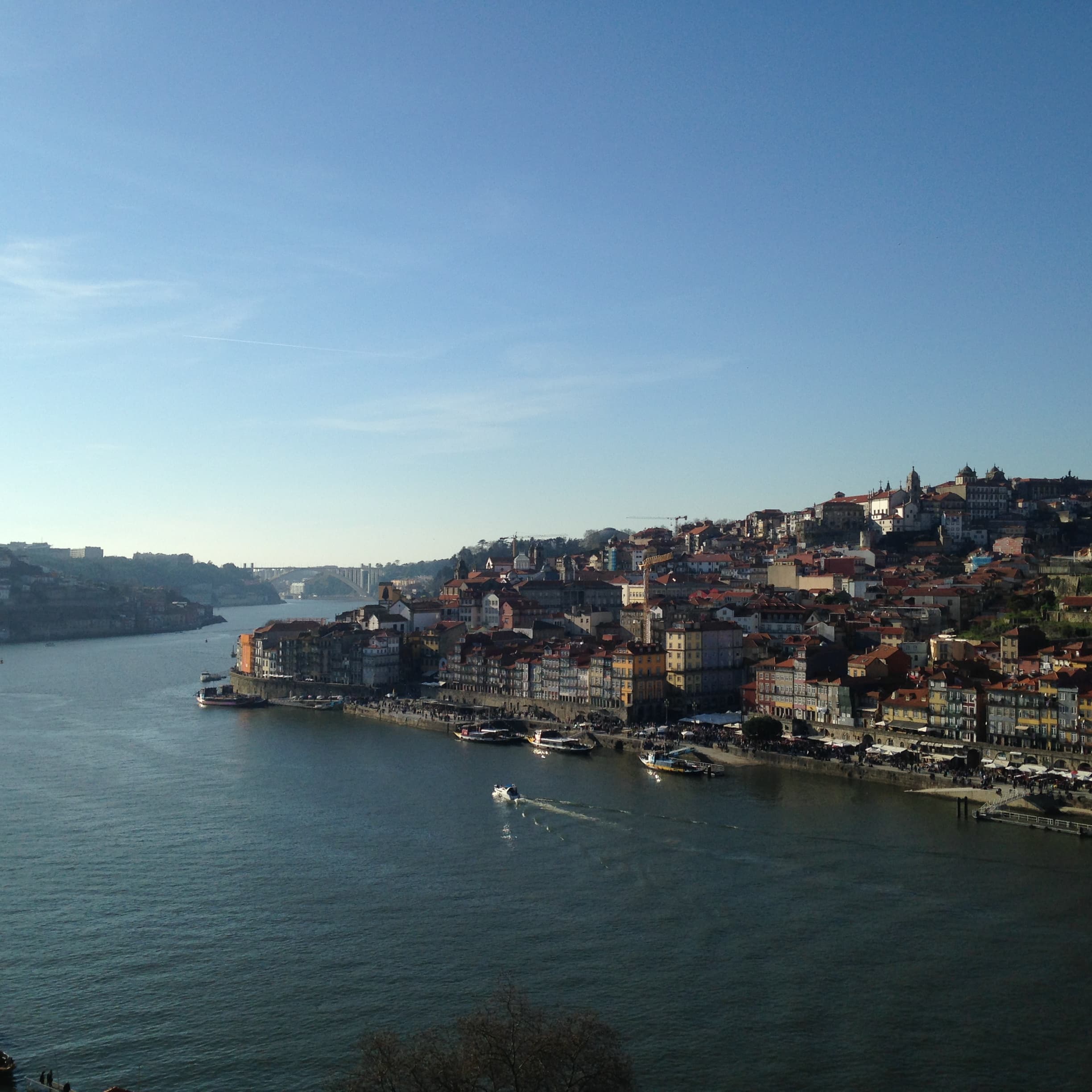 The city of Porto lays in wait out an open window framing a historic church with the view of the water below on a clear day.