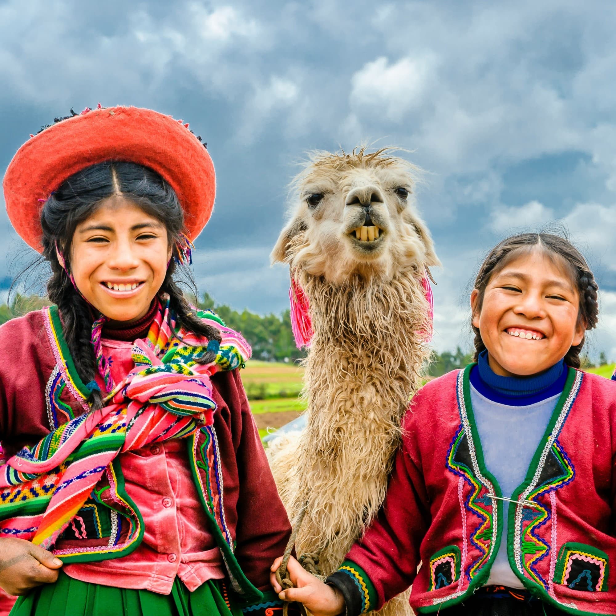 The image shows three individuals in traditional Andean clothing with a llama, set against a cloudy sky backdrop.