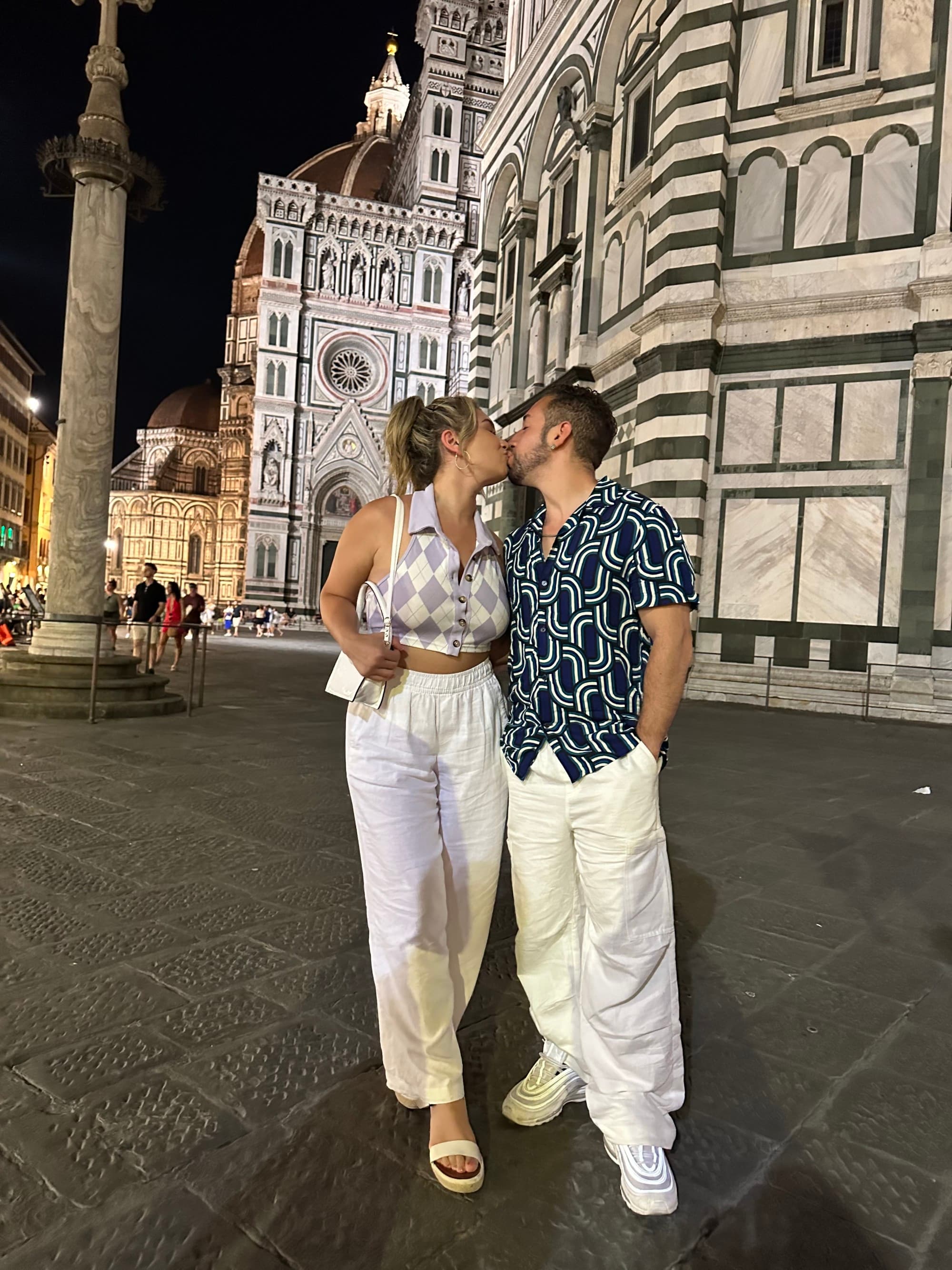 Couple posing in front of historic architecture on a quaint street corner in the evening.