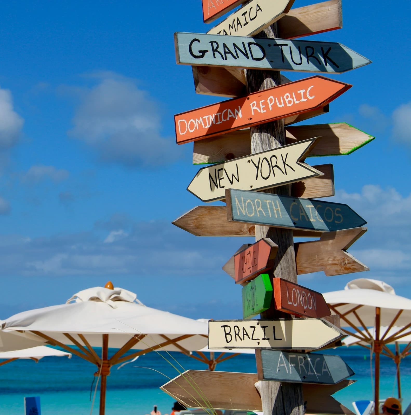 Signages pointing in different directions towards major cities and white patio umbrellas in the seashore of Providenciales.