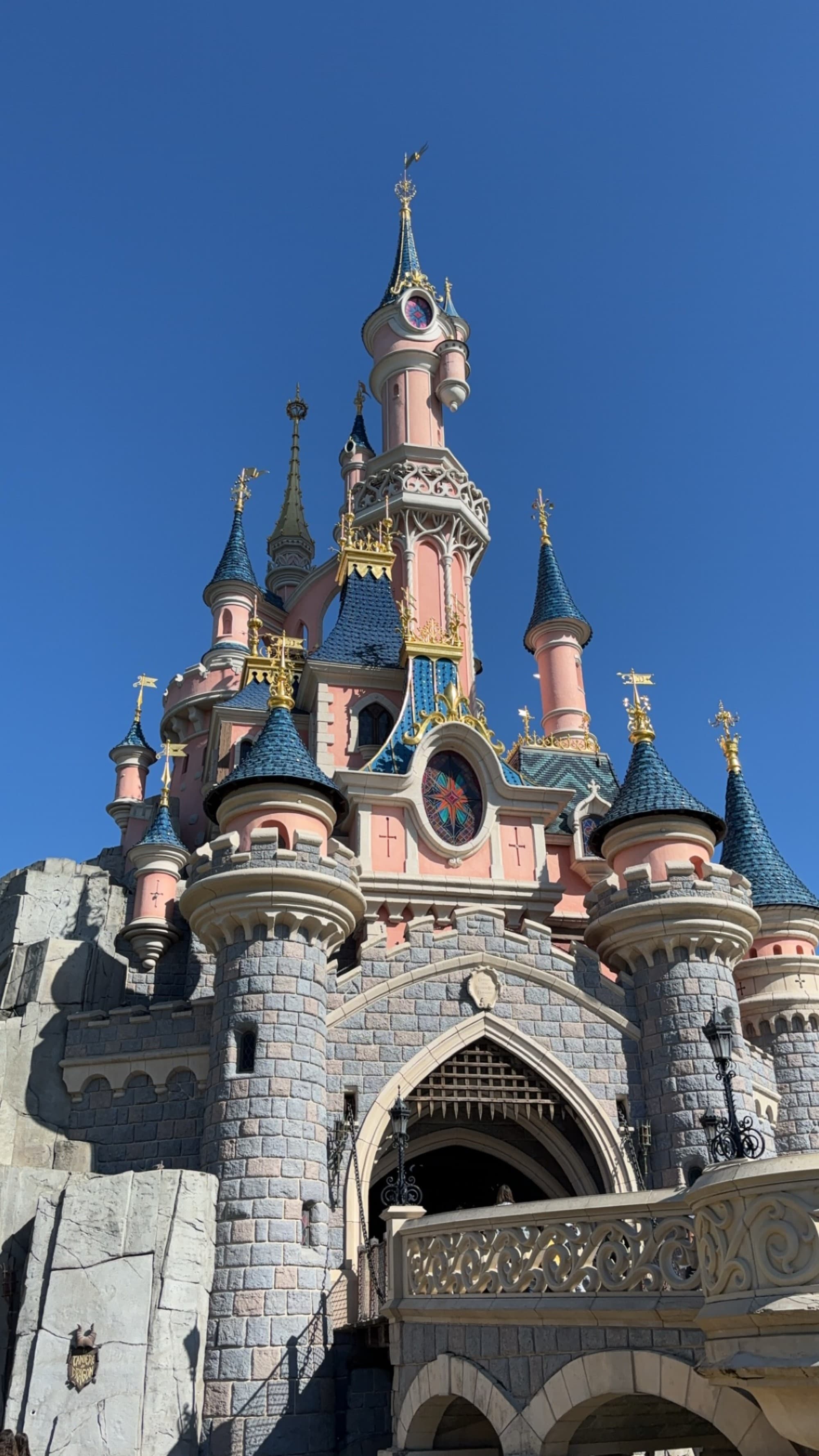 The image depicts the iconic Sleeping Beauty Castle under a clear blue sky at Disneyland Paris.