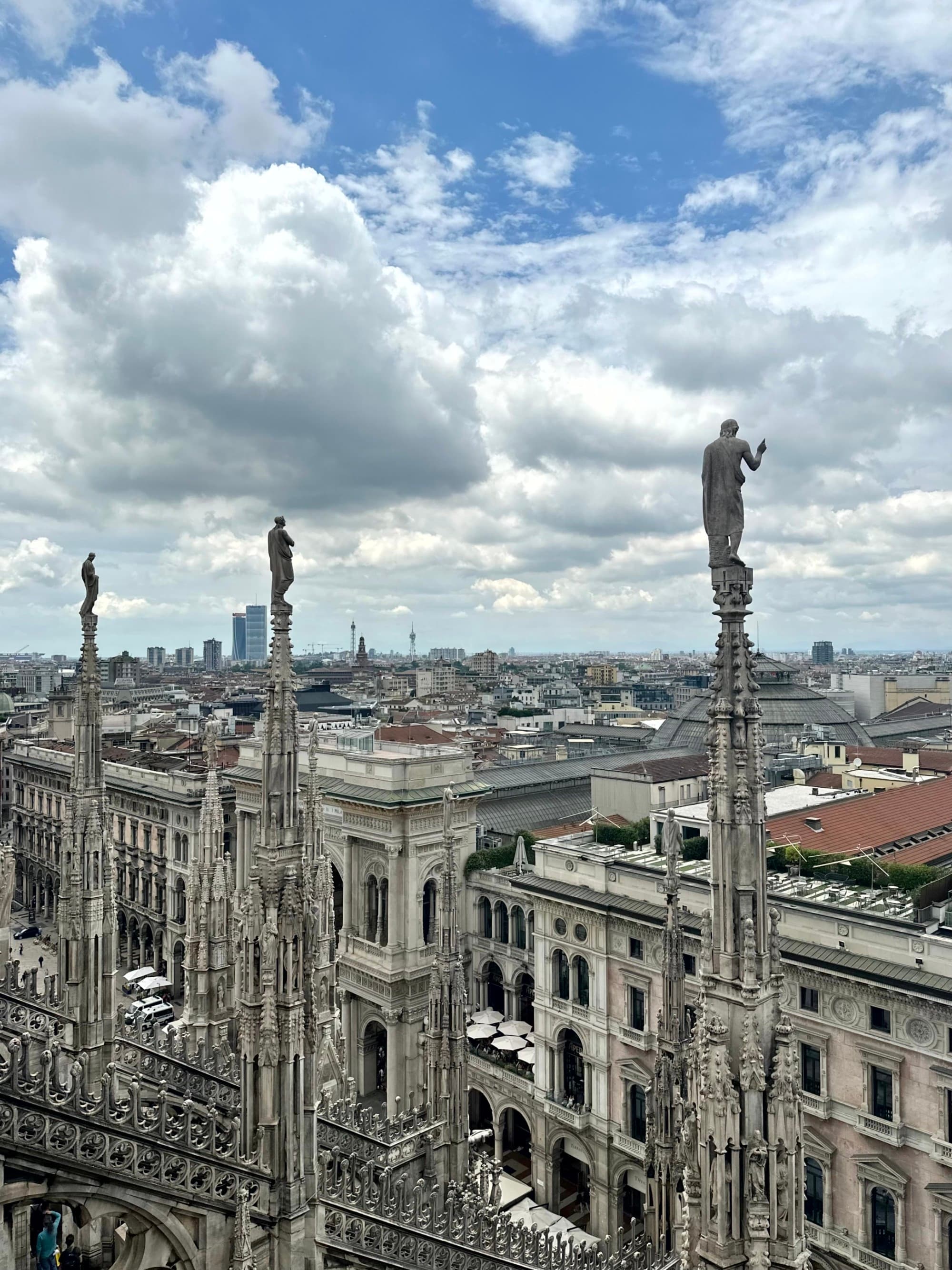 The image offers an aerial view of a cityscape with intricate gothic architecture in the foreground under a cloudy sky.