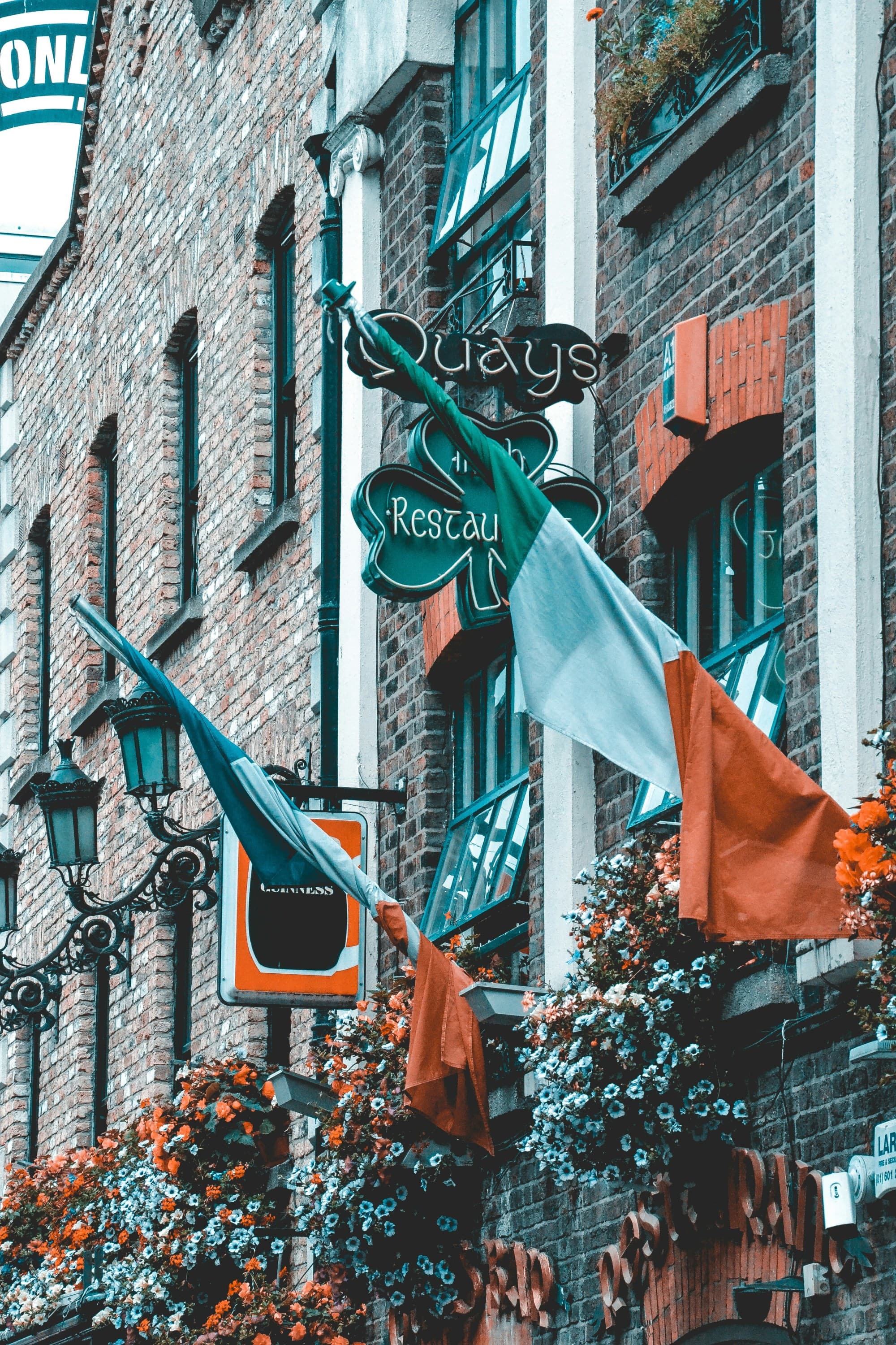 The image presents a vibrant urban scene with flags, a neon sign, and a brick building, exuding a distinct teal and orange street aesthetic.