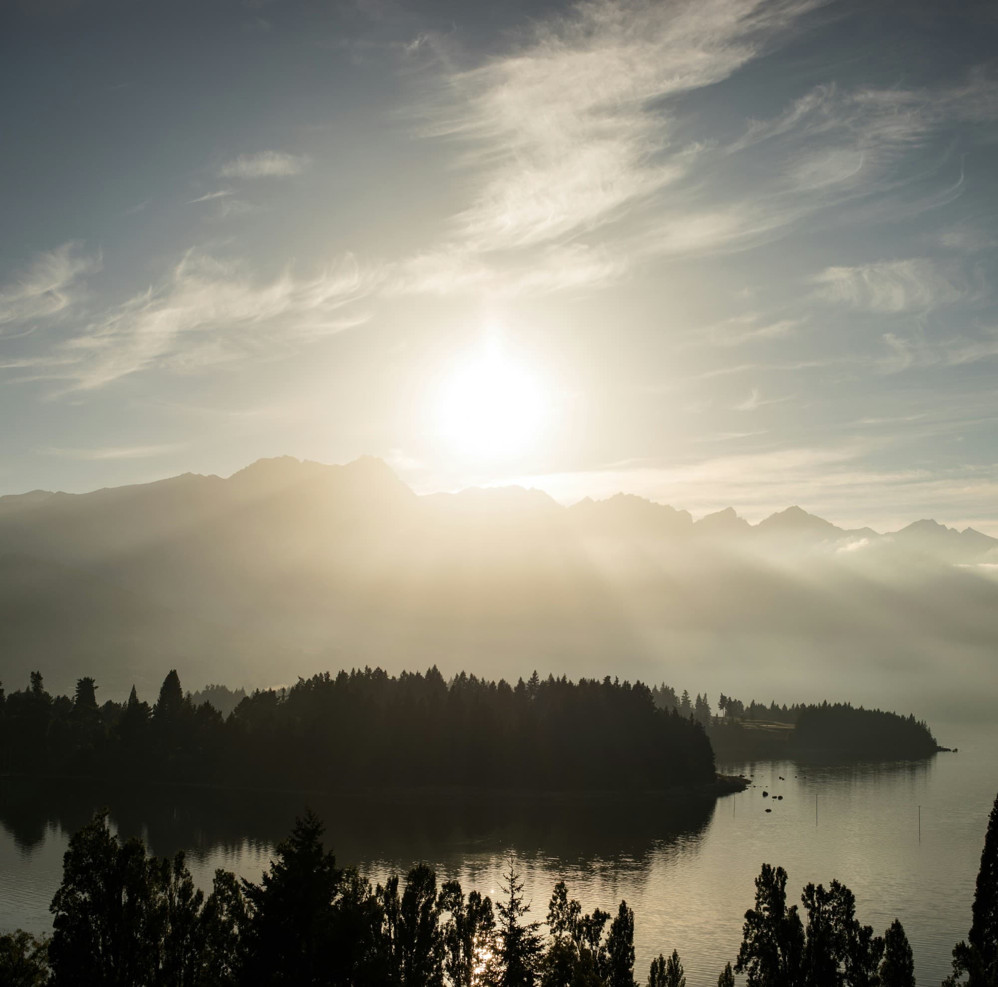 The sun's rays glide over dense foliage and clear waters and wisps of clouds drift overhead.