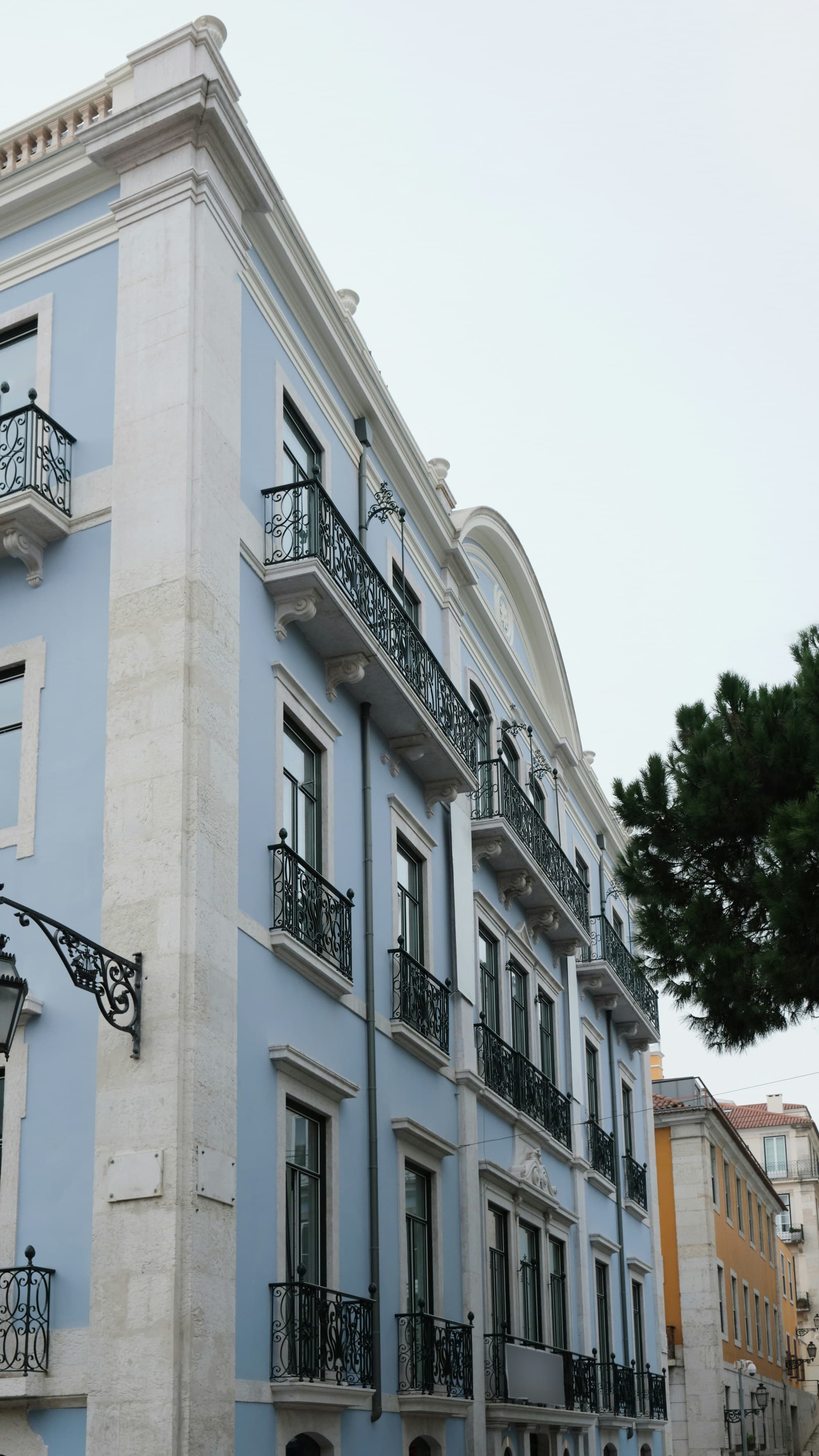 A charming building with blue walls, white trim, and ornate black balconies with arched windows.