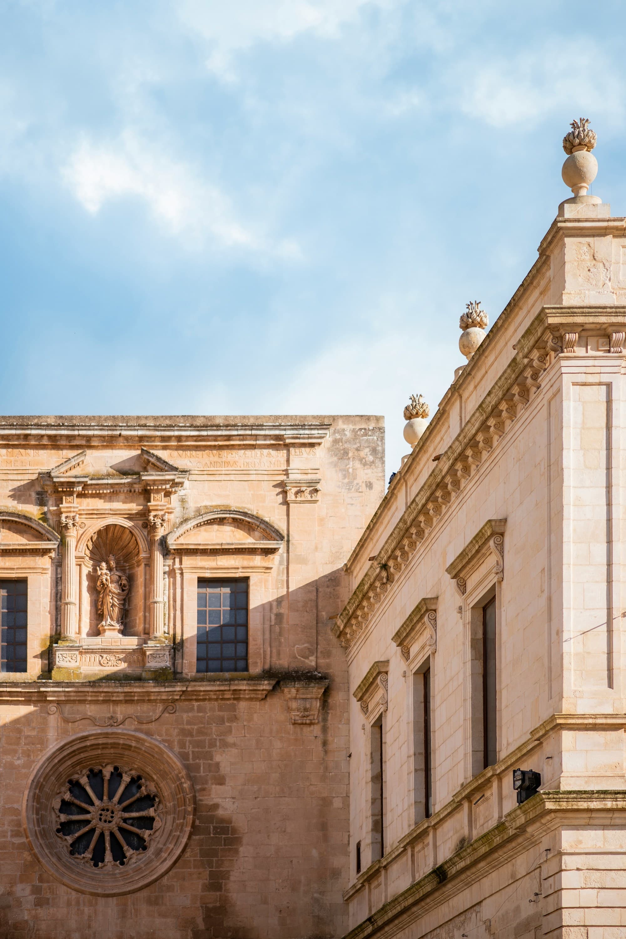 The image features the intricate architecture of a historic building with elaborate stone carvings set against a backdrop of a blue sky with clouds.