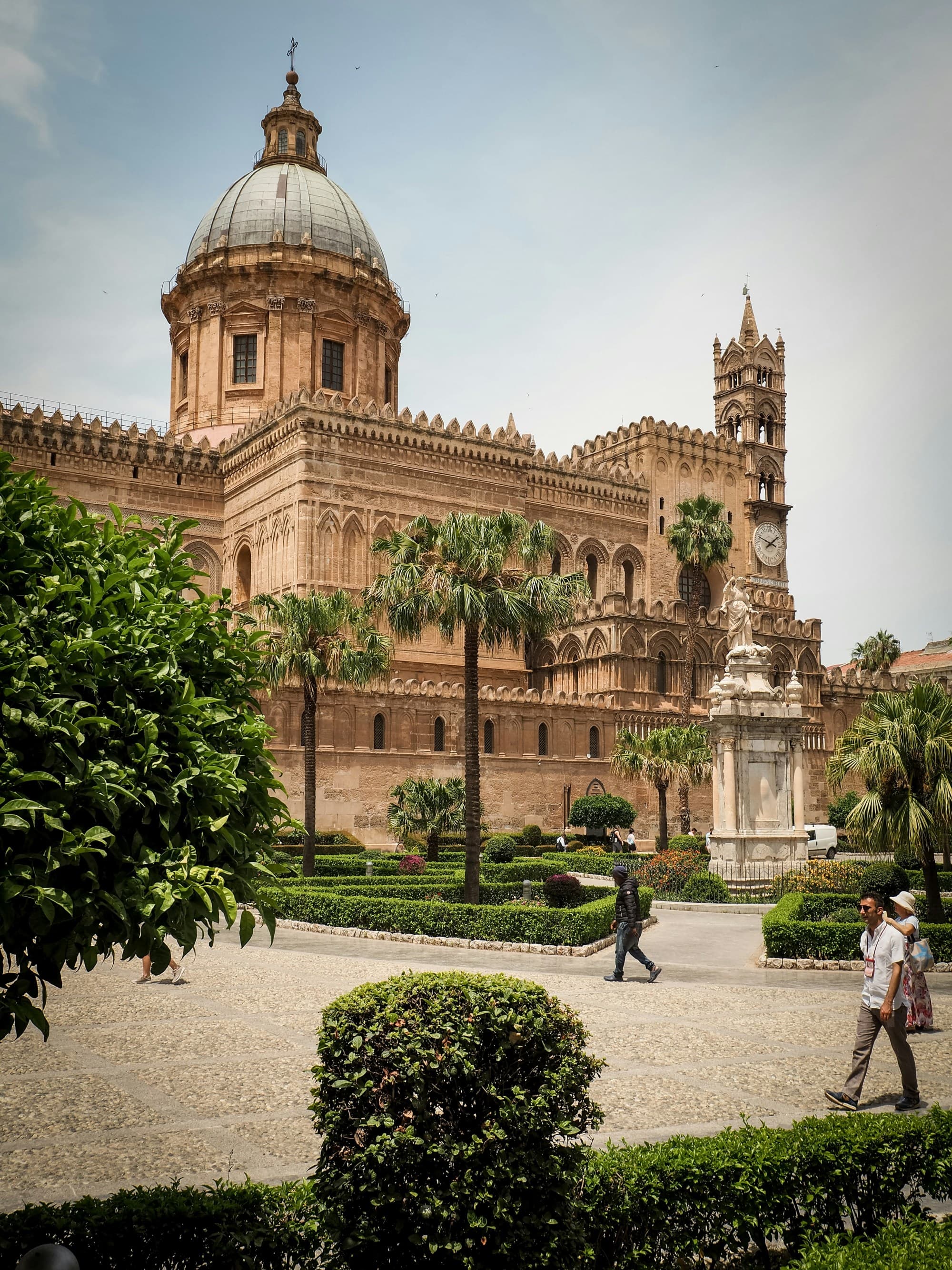 The image features a grand cathedral with a dome, surrounded by a garden and people, under a clear sky.