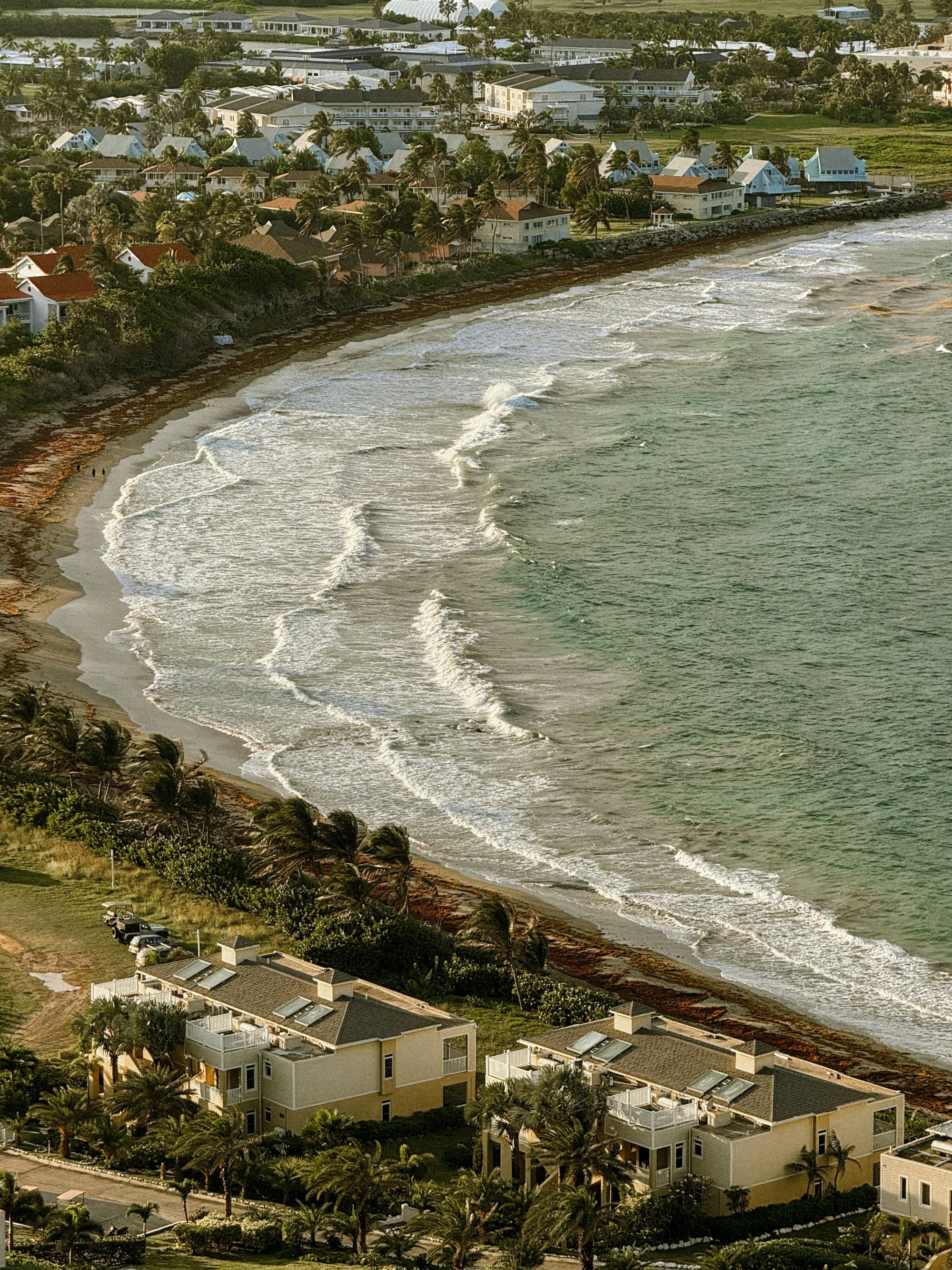 The image depicts a serene coastal scene with houses along the shoreline and waves gently approaching the beach.