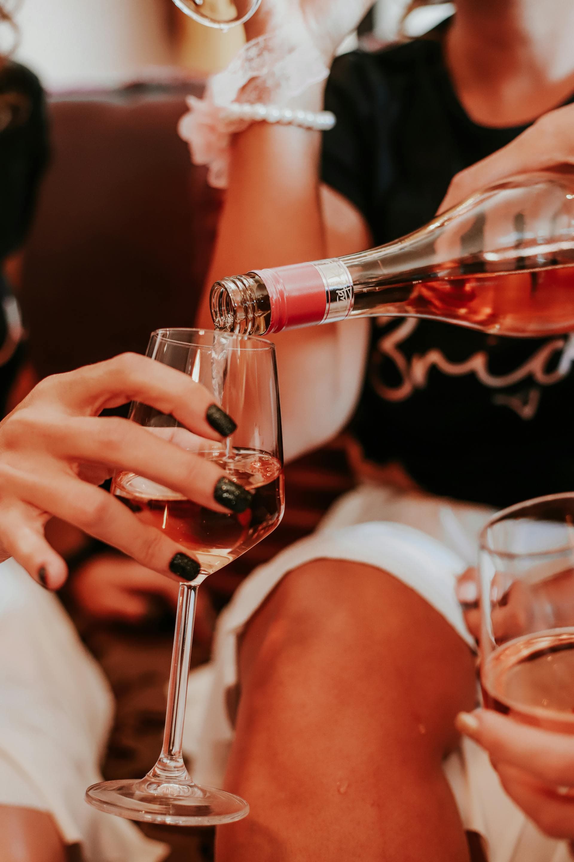 Friends raise a bachelorette toast filling glasses with rosè in a cozy corner.