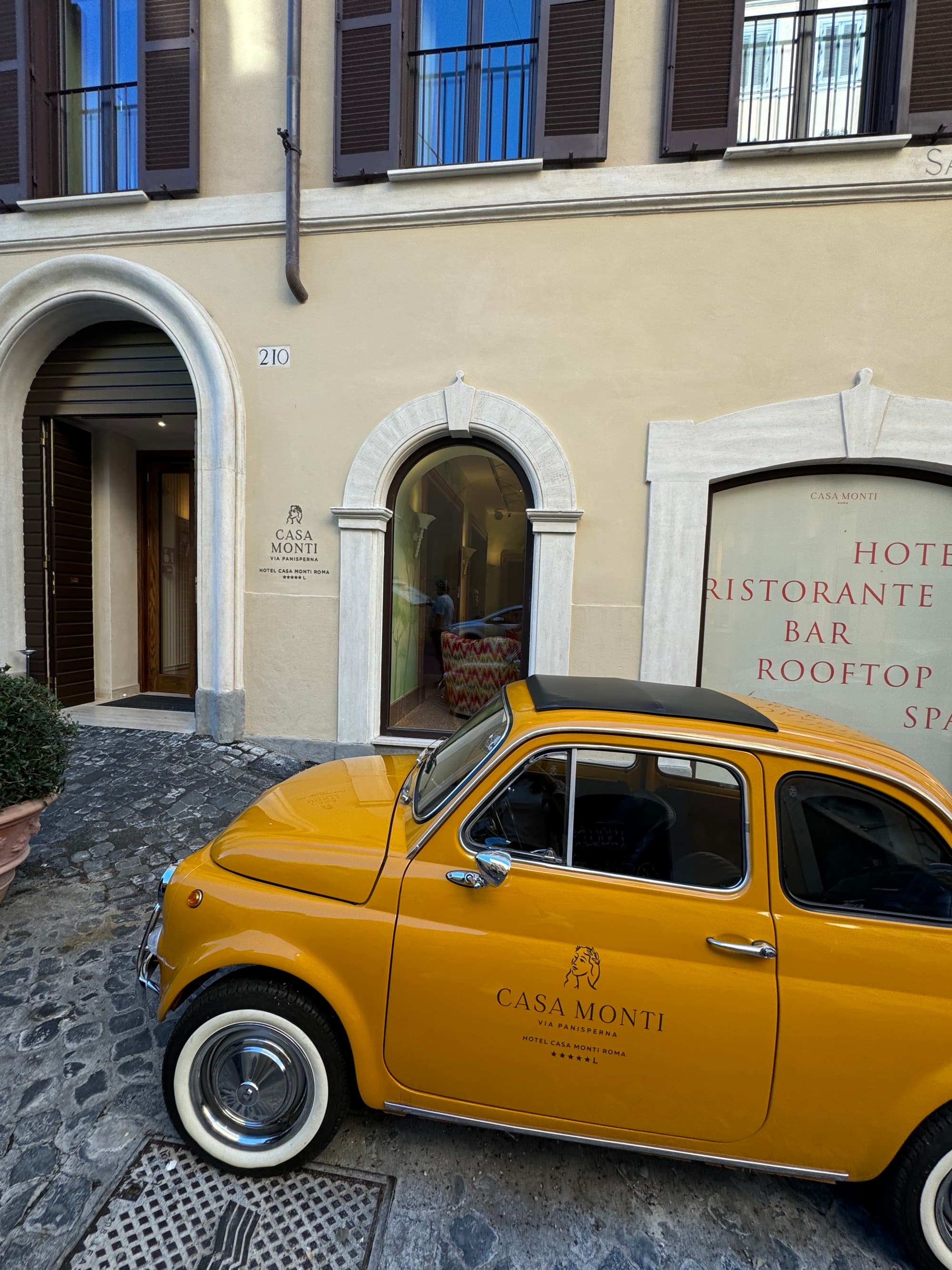 A view of a small yellow compact car parked outside of the hotel.