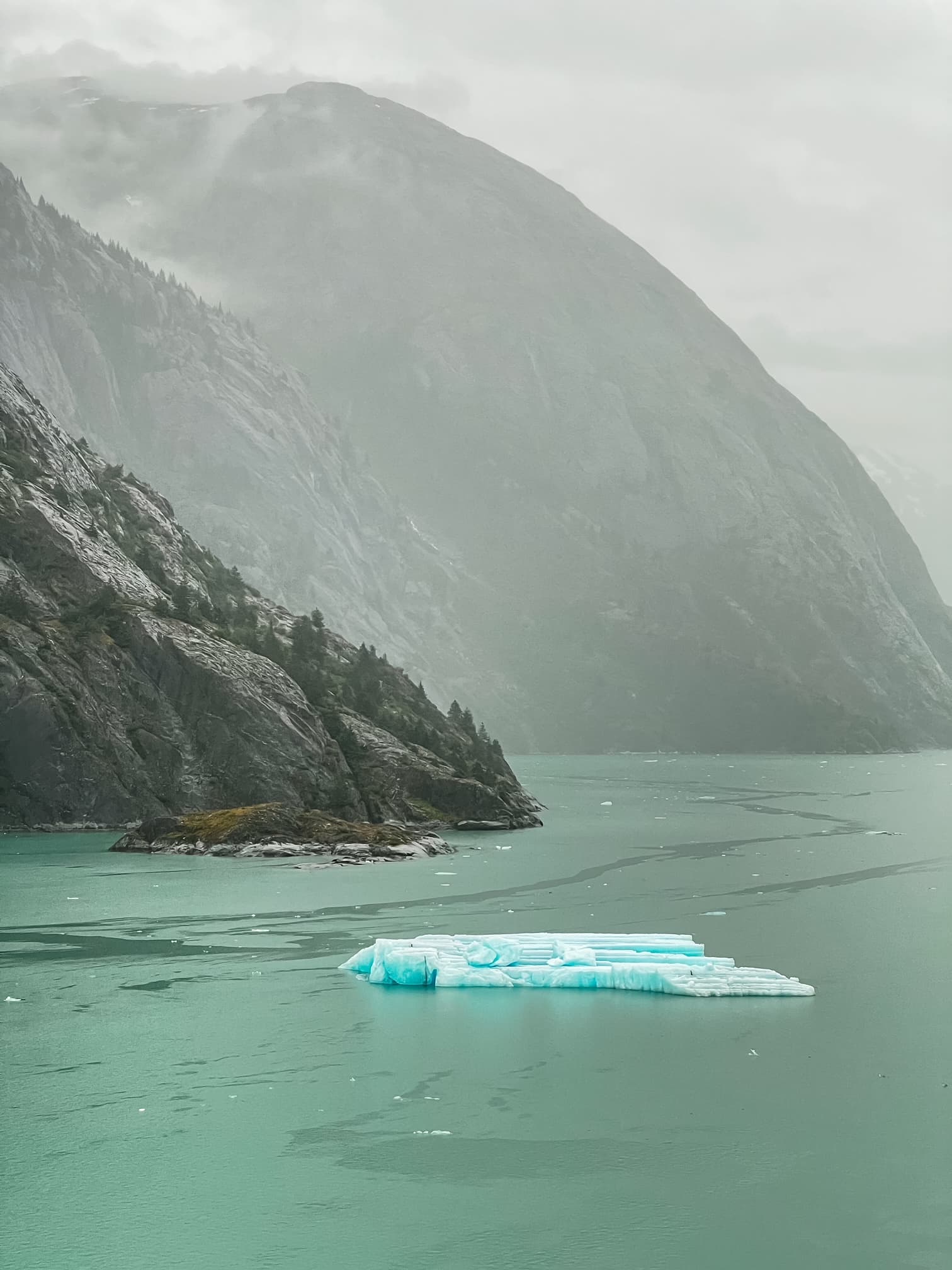 A view of the ocean as waves lap against a rocky shore on a misty day.