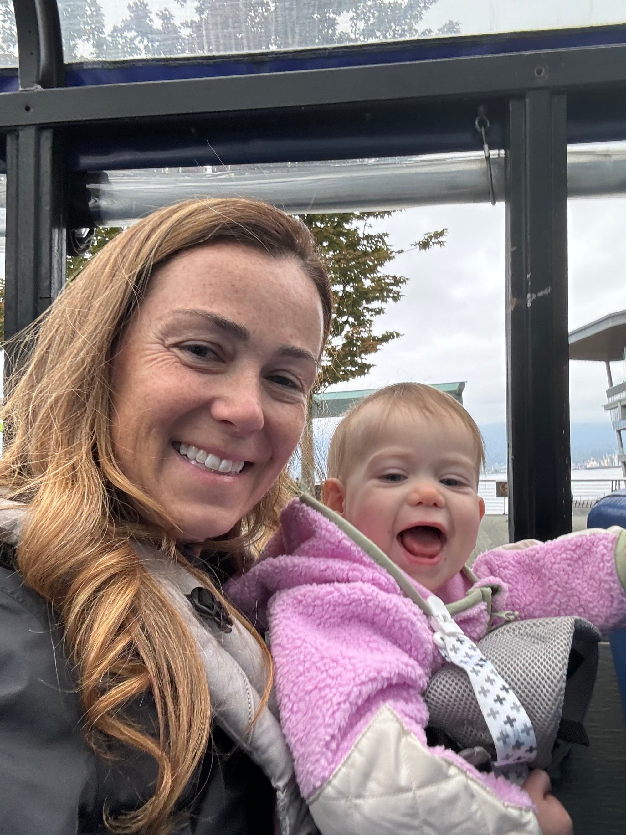 A mother and child on her lap, both smiling at the camera. Behind them a window looking outside.