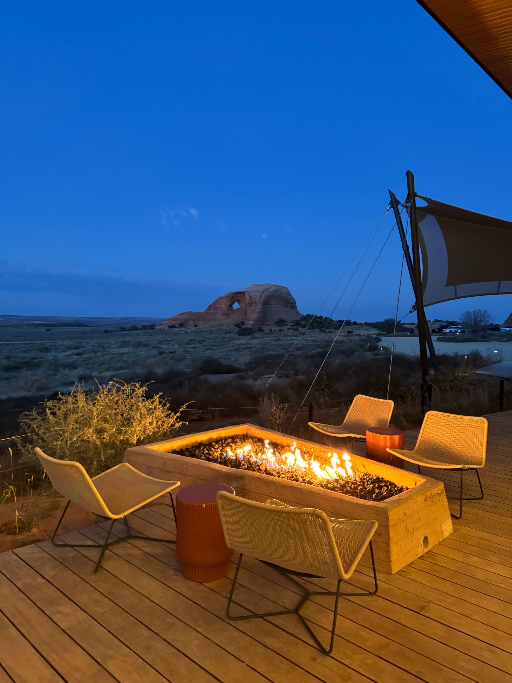 A view of an outdoor seating on a wooden deck with chairs surrounding a fire pit at dusk.