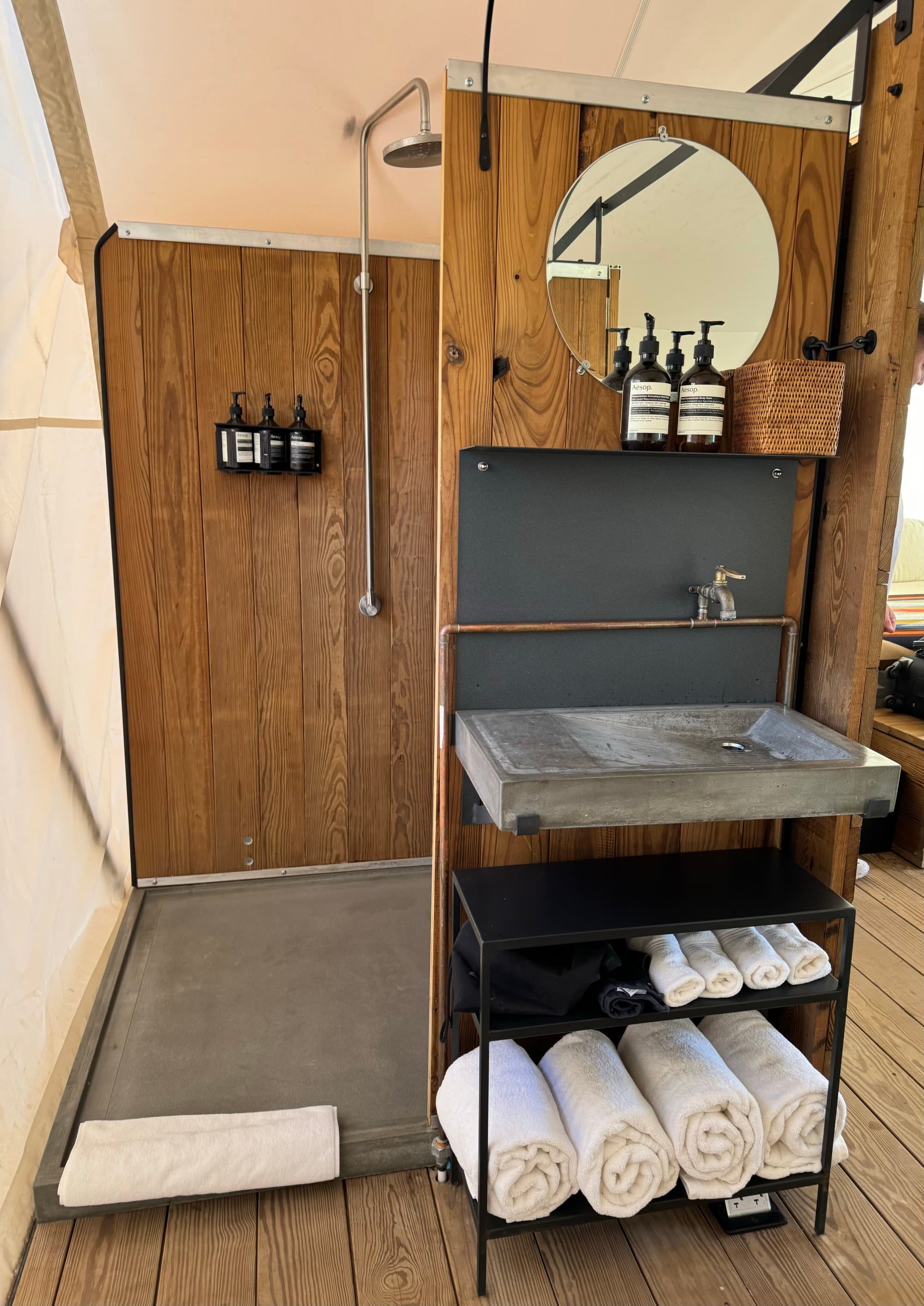 A bathroom with a standing shower, wood slat walls and a cement sink.