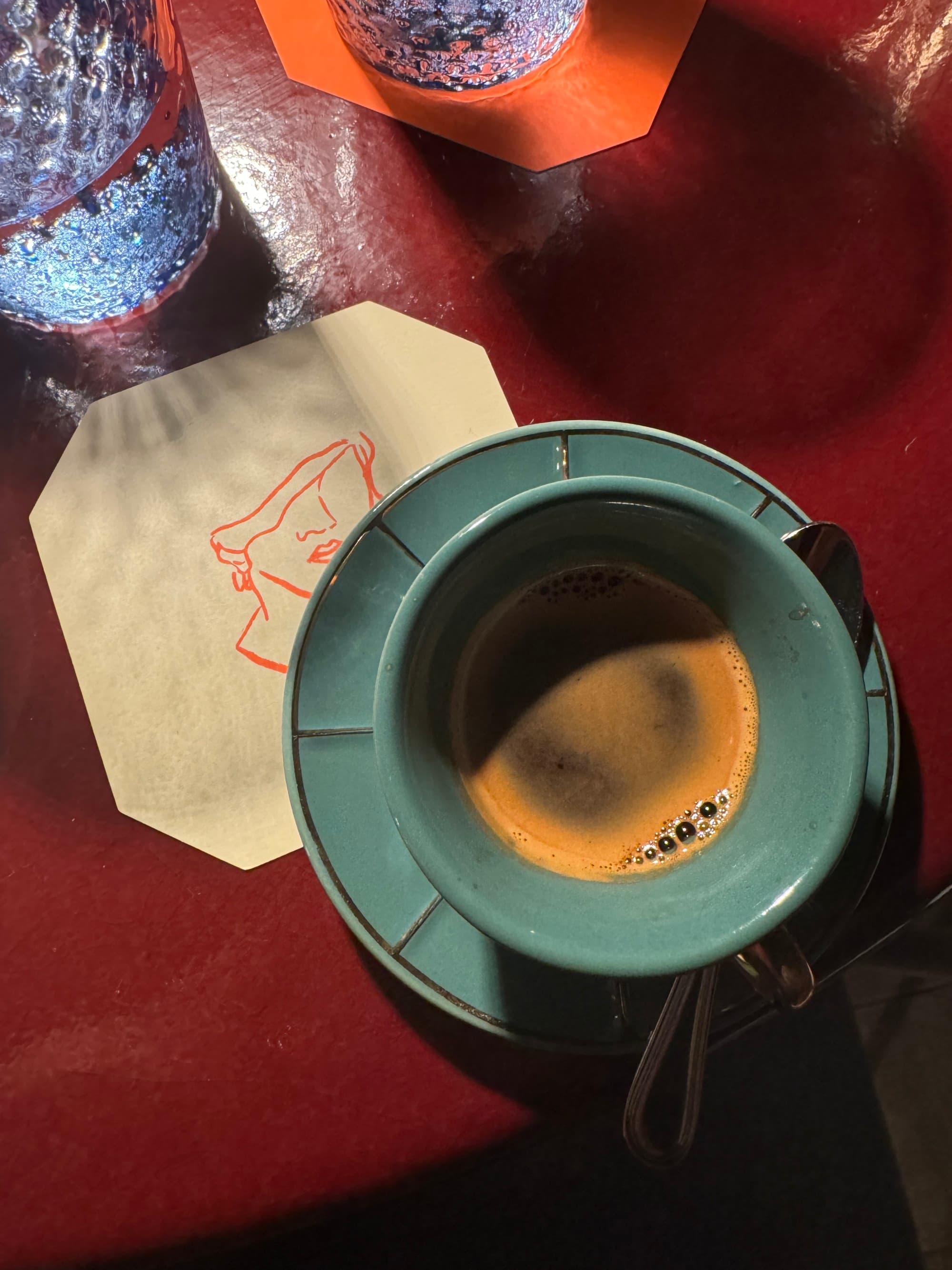 A view looking down on a teal coffee cup on the red table with a napkin beneath it.