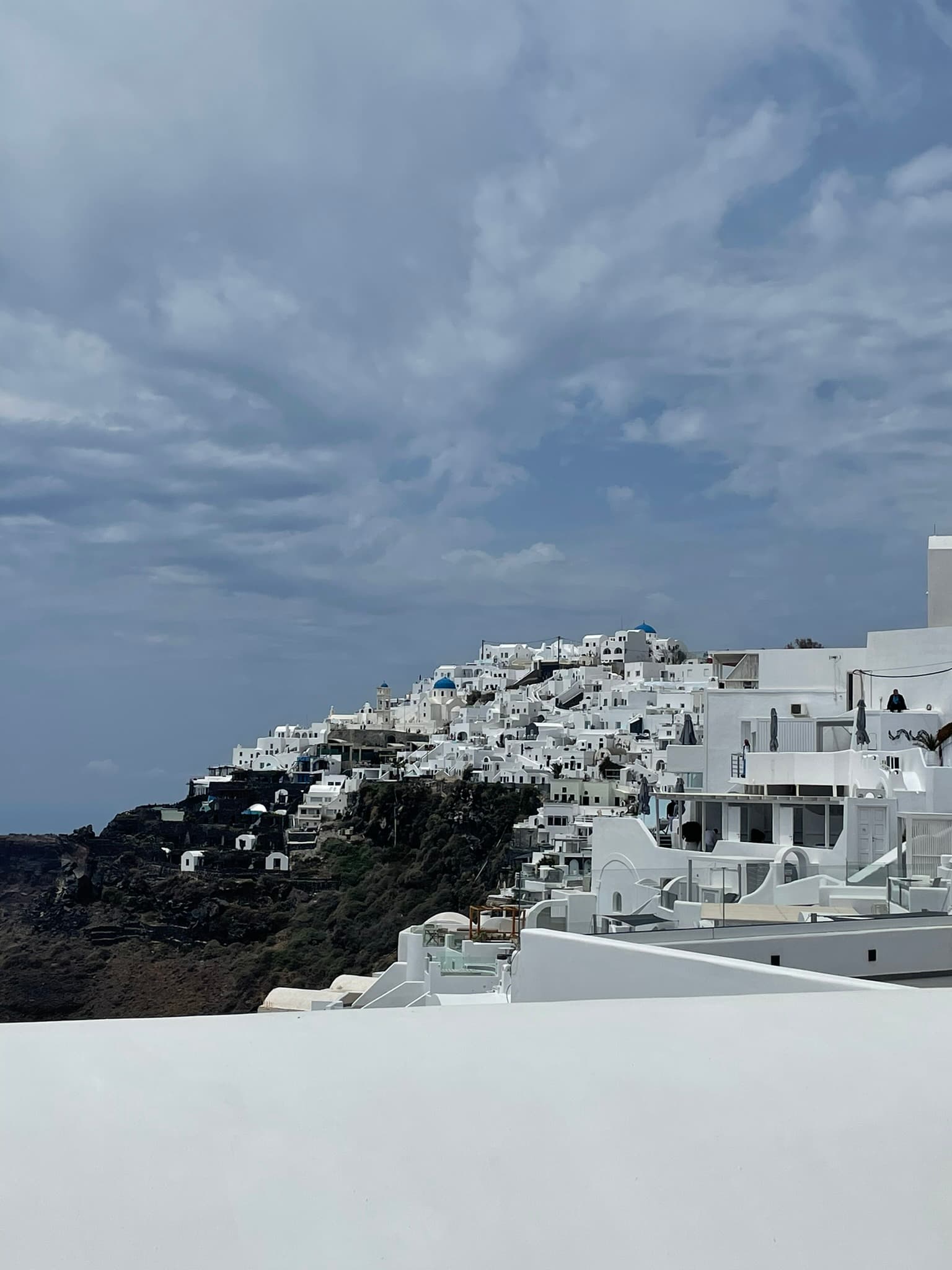 White village buildings stand tall against a blue sky dotted with clouds along the hillside shore.