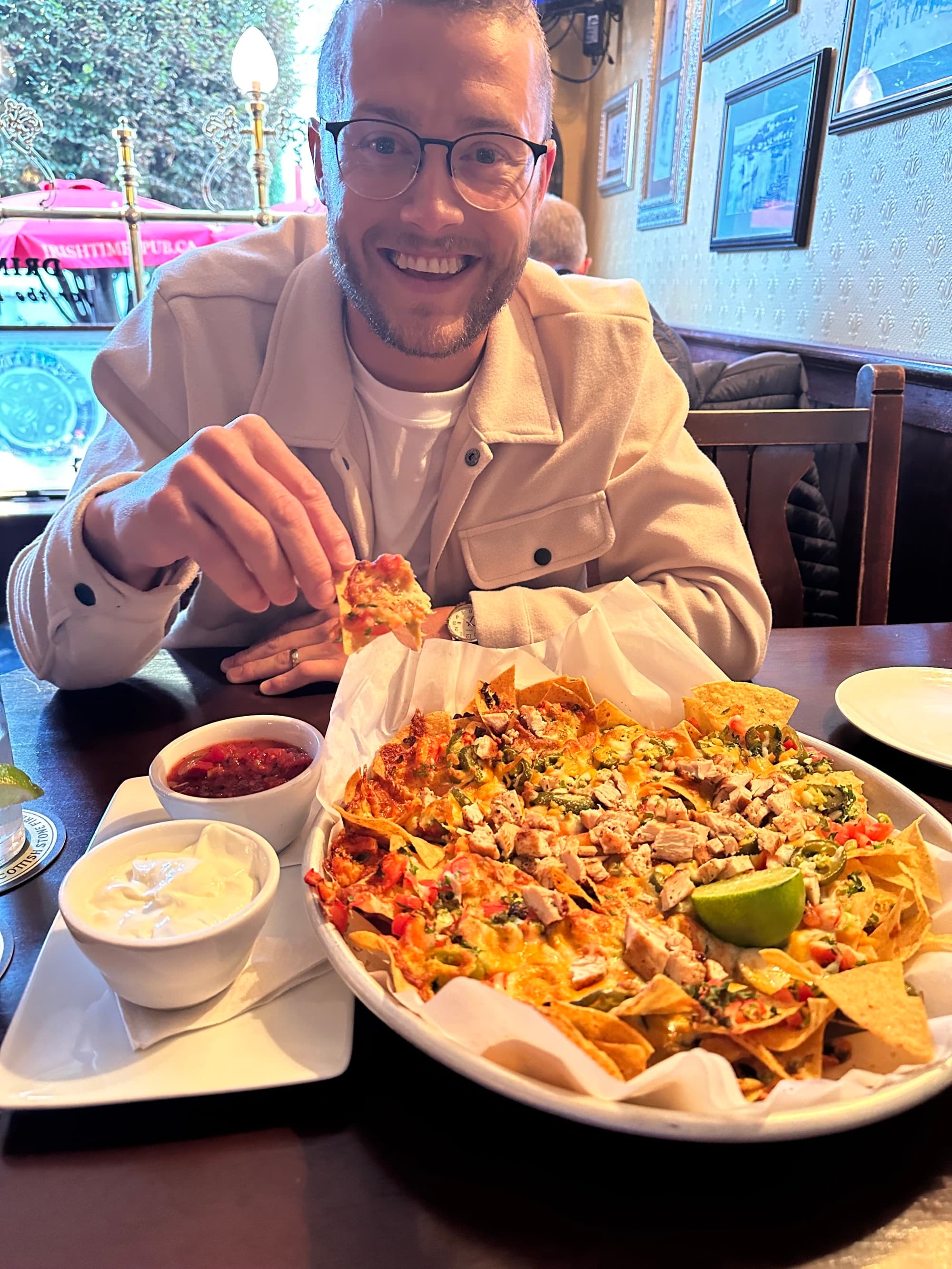 A person in a restaurant in front of a plate of nachos