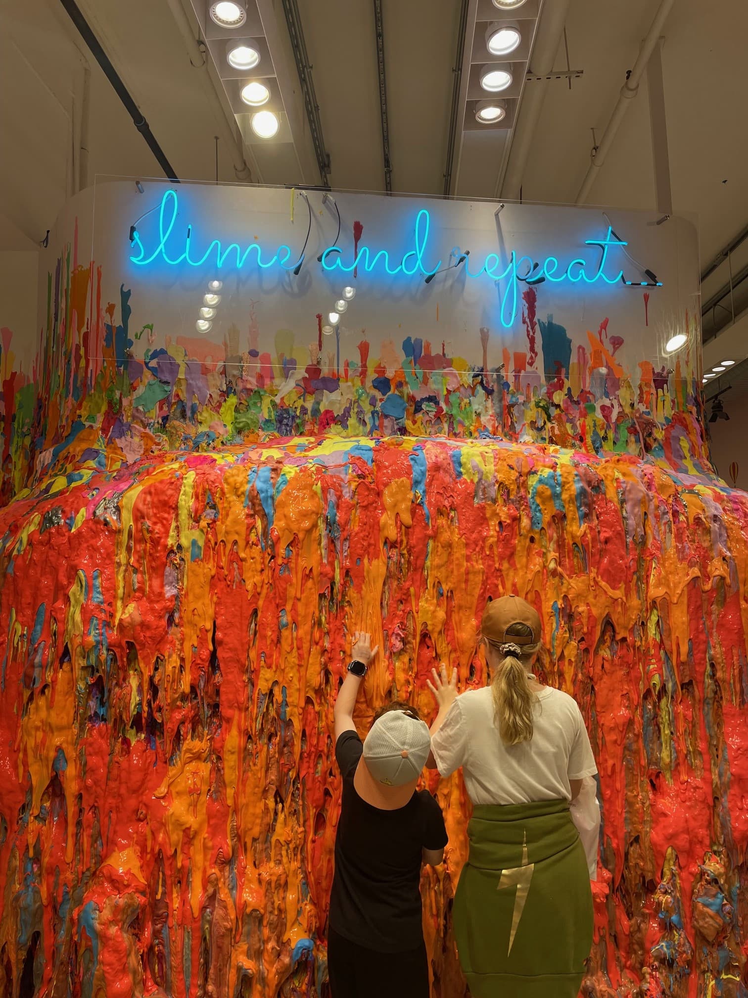 Tourists viewing a slime exhibit reaching from floor to ceiling.