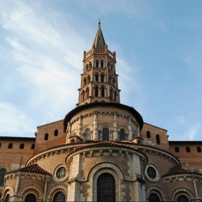 Historic brown building with cross at top against a clear sky and wisps of clouds.