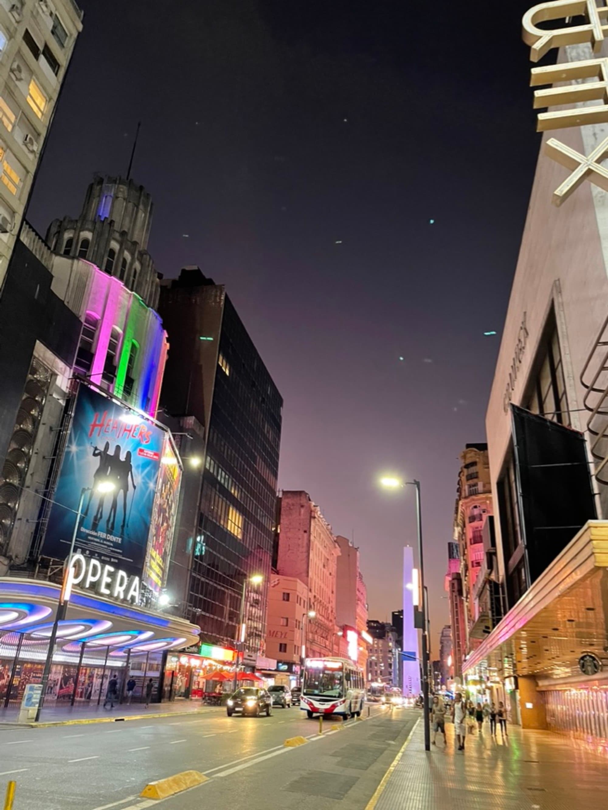 The image depicts a bustling city street at dusk, illuminated by neon signs and lined with buildings.