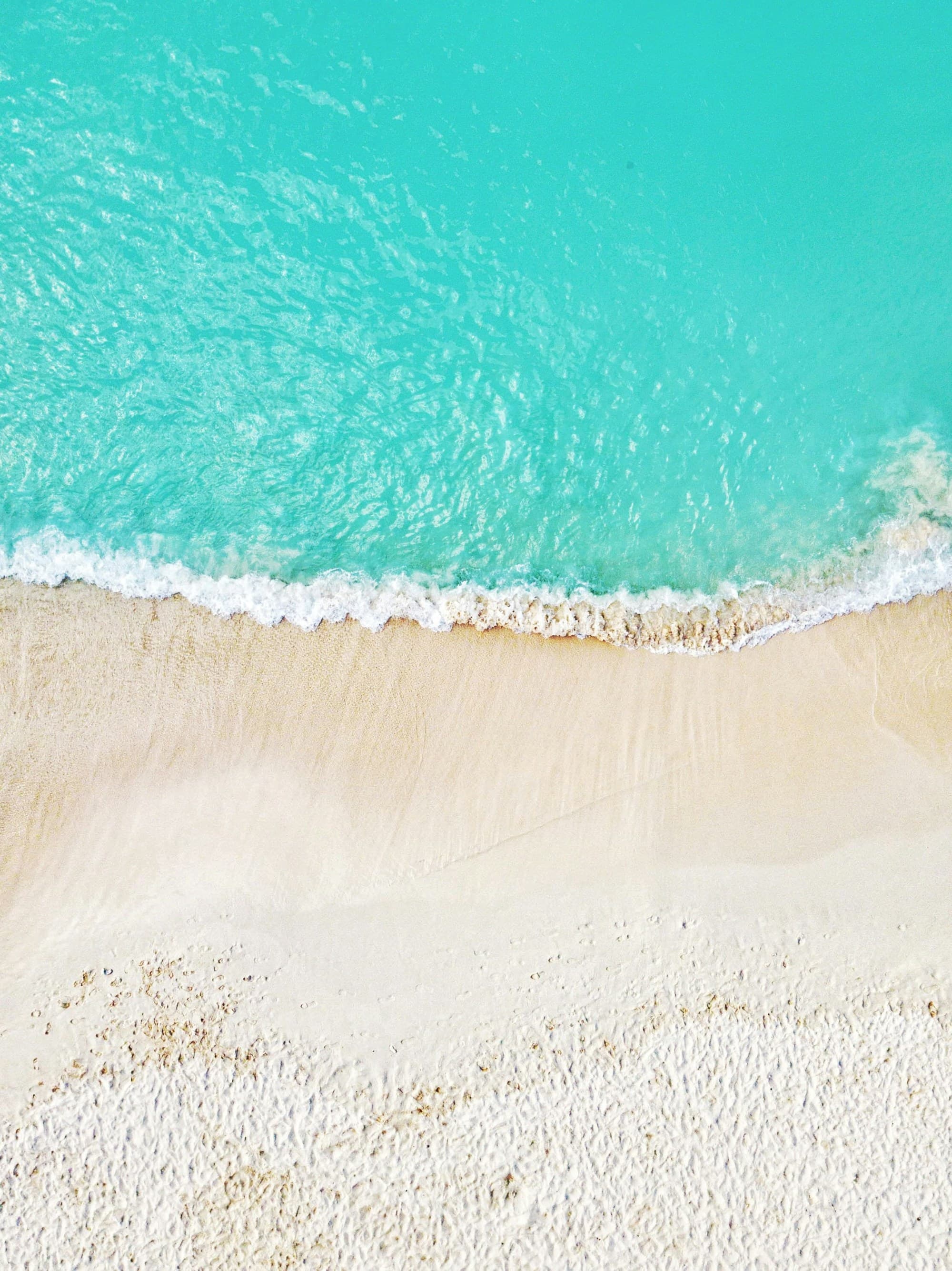 Crystal clear waters roll onto a white sand beach on a sunny day.