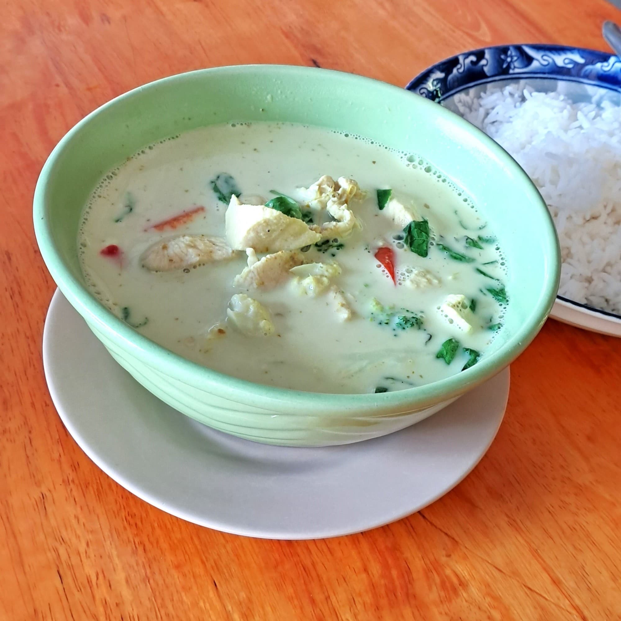 The image features a comforting meal with a bowl of soup and a side of rice on a wooden table.