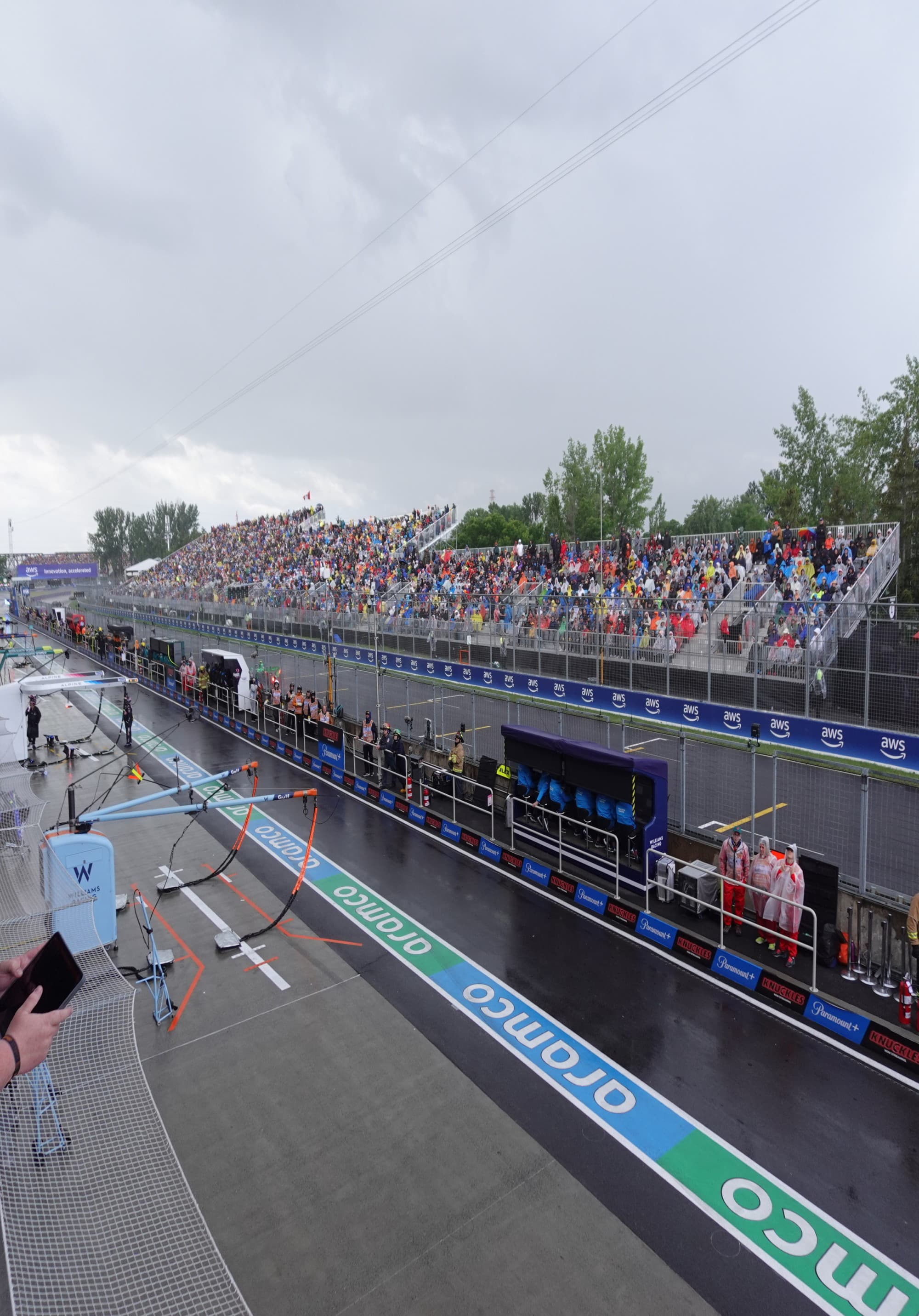 A bustling grandstand overlooks the adrenaline-fueled precision of a motorsport race, under a sky hinting at the unpredictability of nature.